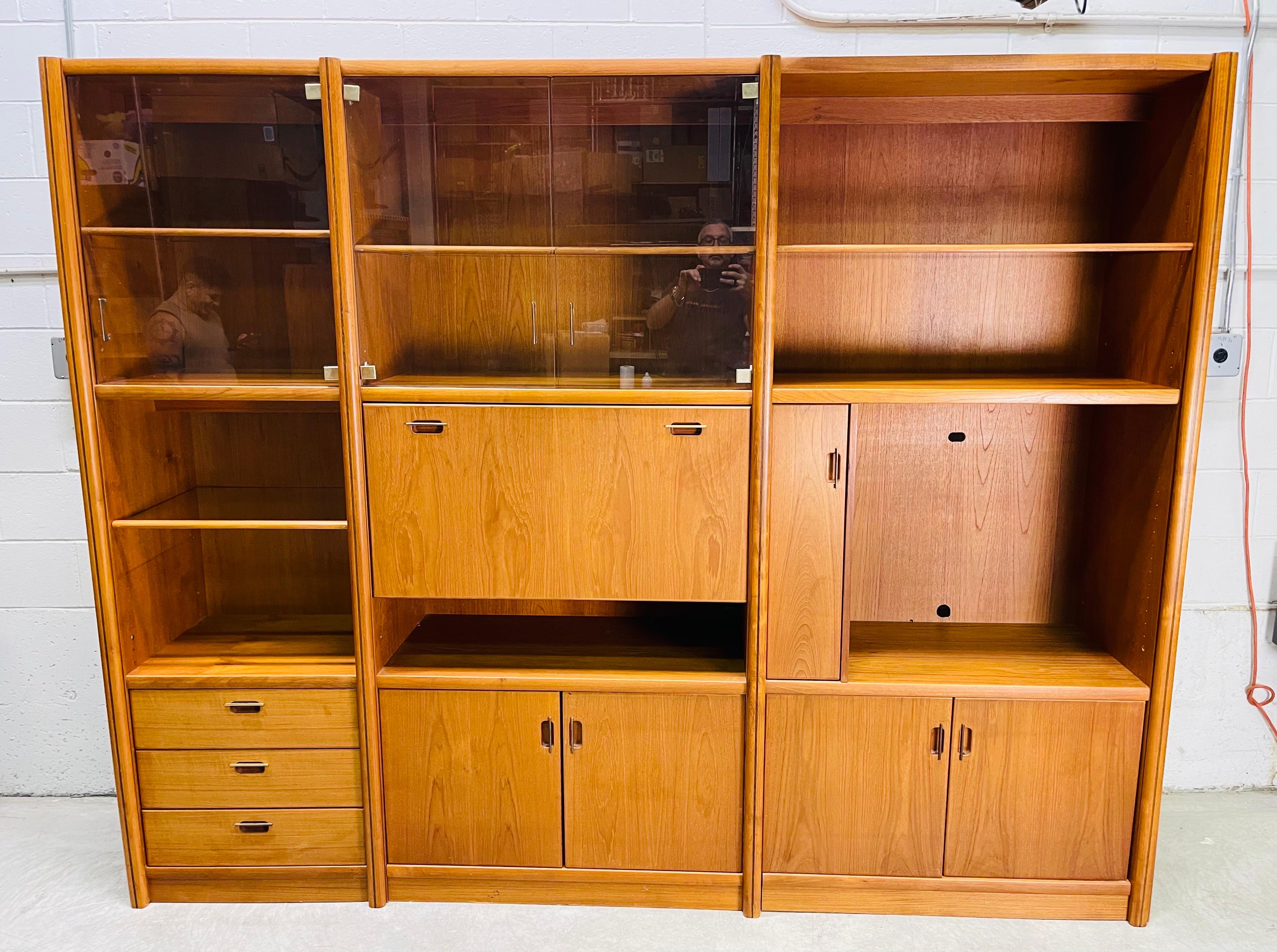 Vintage 1980s teak wood three-section living room entertainment center. The unit comes with glass shelves, drawers, a desk writing area, TV area and glass doors with areas to display items. Many of the shelves are adjustable. The unit is in three