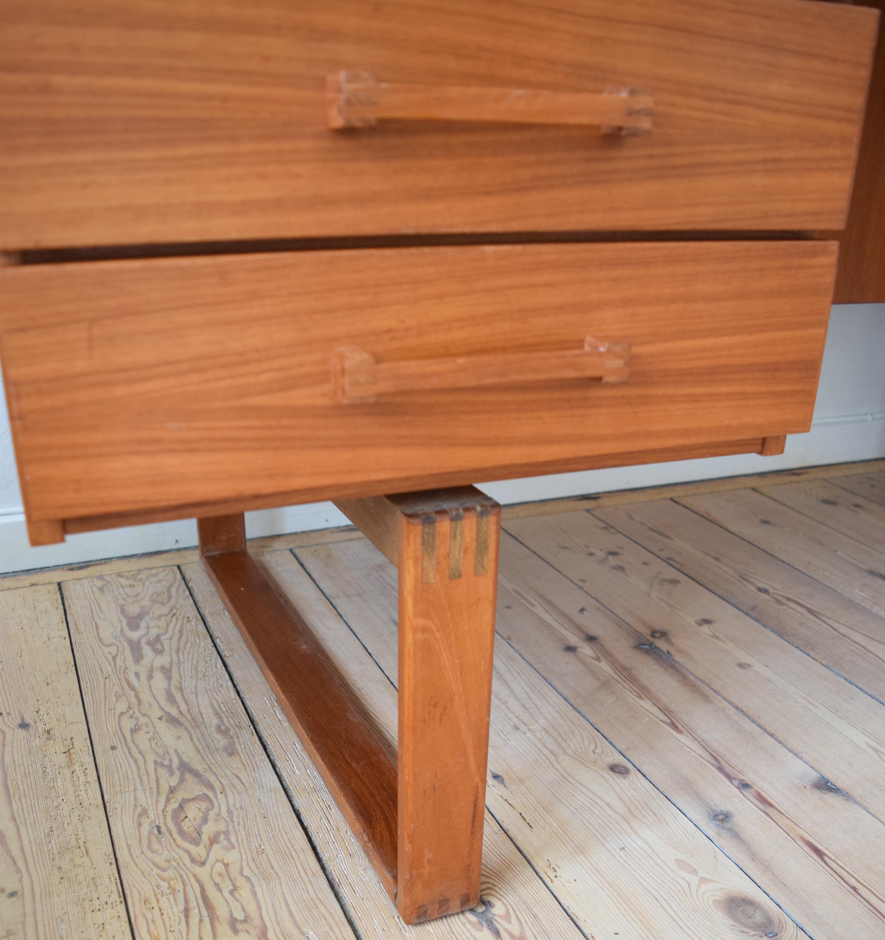 Teak executive desk designed by Henning Jensen & Torben Valeur in the 1960s, featuring 6 drawers with solid teak handles. Large book compartment on rear side. Sits on teak spade legs with exposed finger joint construction. Raised lip on rear edge of