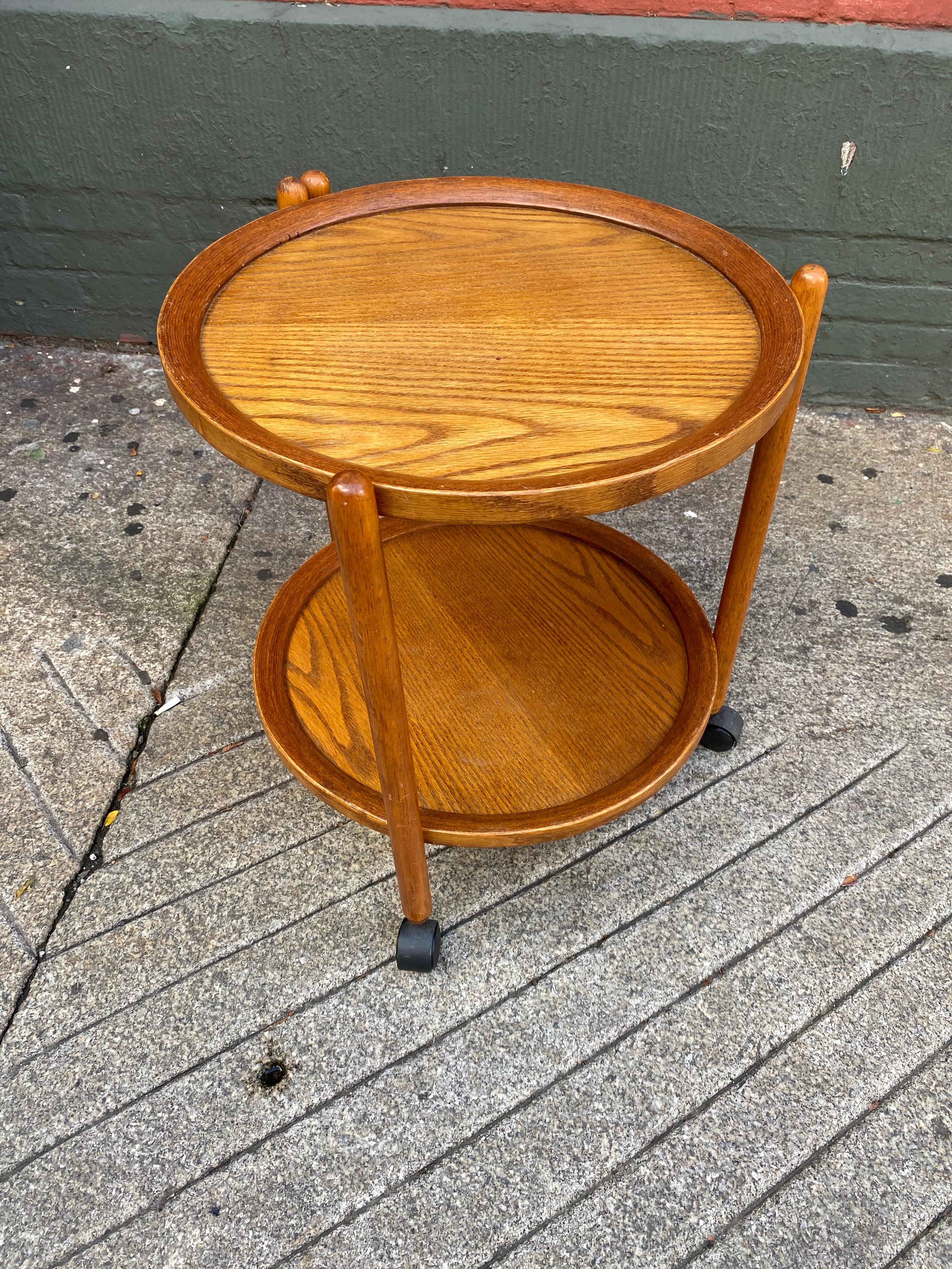 Teak folding round bar cart. Frame folds and both trays can be removed for serving or storage. Triangular design cleverly gives ample support to the cart. Easily moves on it's wheels.