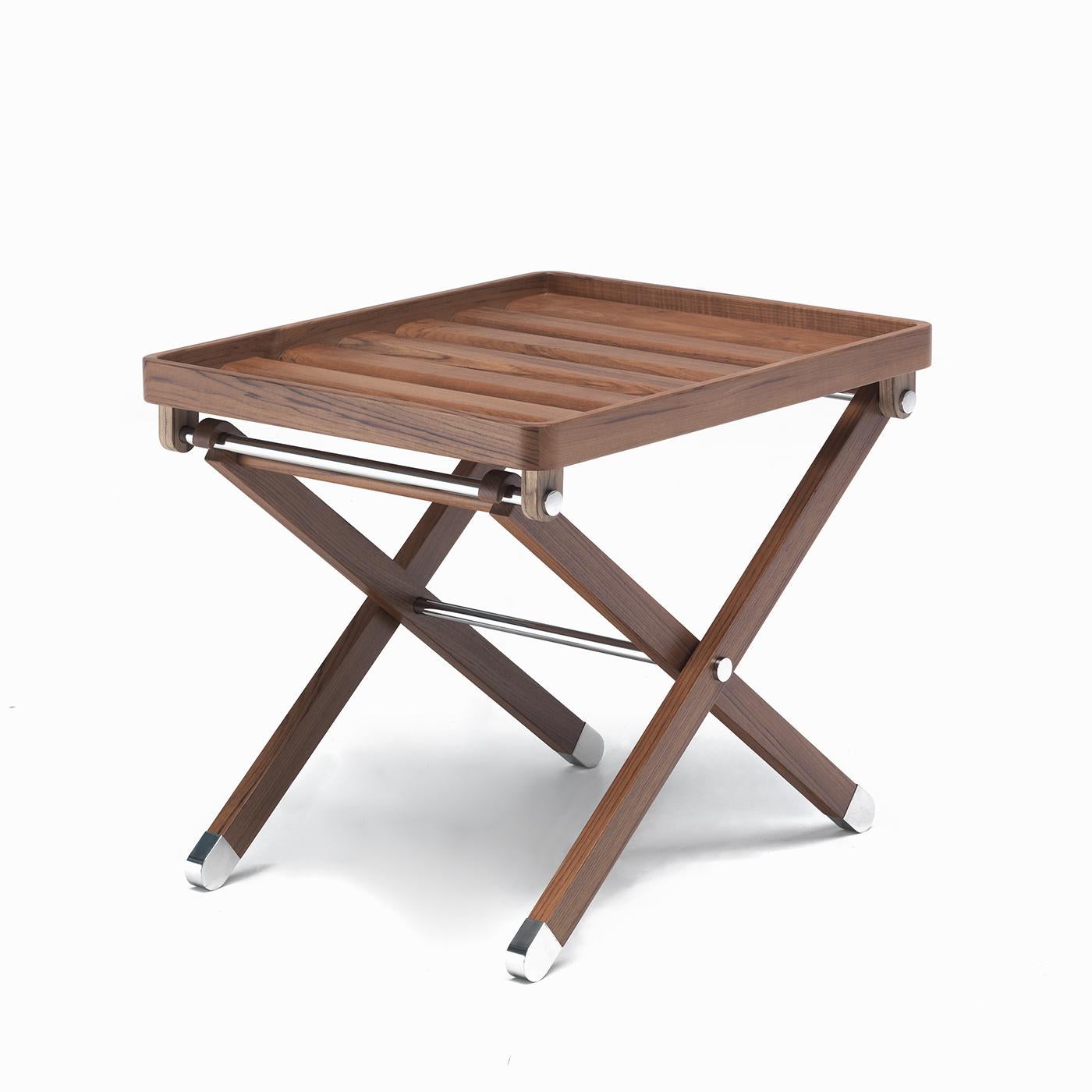 Con una silueta tan elegante como elemental, esta mesa plegable es la pieza de mobiliario ideal para añadir una superficie de servicio adicional allí donde se necesite sin renunciar al estilo. La estructura combina teca y acero inoxidable,