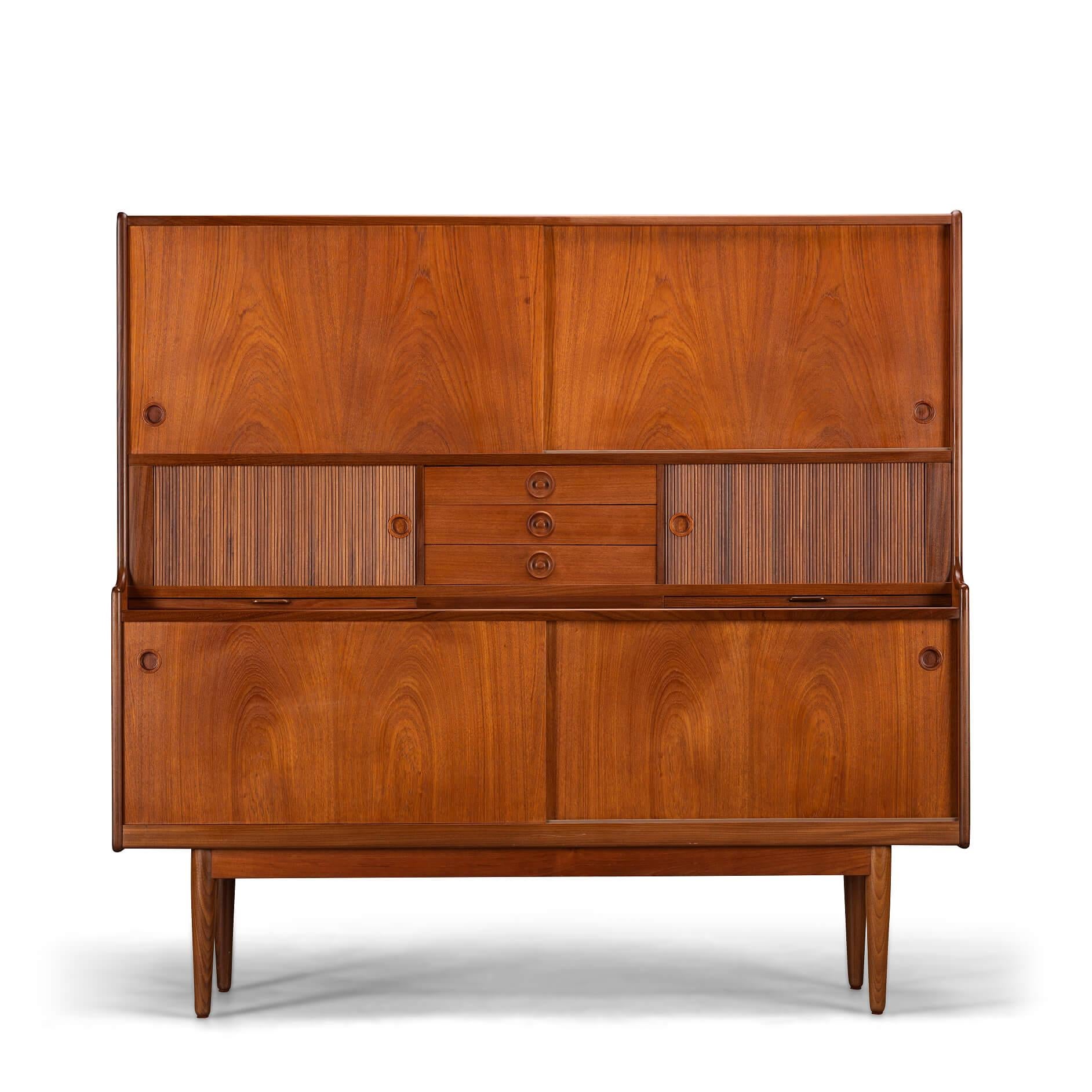 Storage Galore on this teak highboard made by J. Skaaning & Søn and designed by Johannes Andersen in the early 60s. It comes with all you covet in a vintage high board such as shelves, a glass lined and mirror equipped wopping bar section, pull out