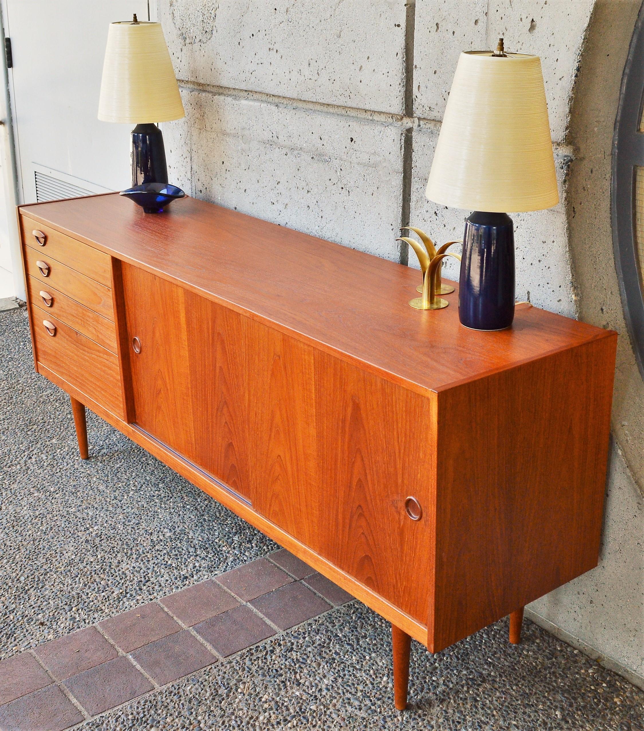 This totally hot Danish modern teak buffet or credenza was designed by Kai Kristiansen in the 1960s with a bank of 4 drawers on the left with his iconic sweet smile shaped sculptural drawer pulls. The top three drawers are more slender, the lowest