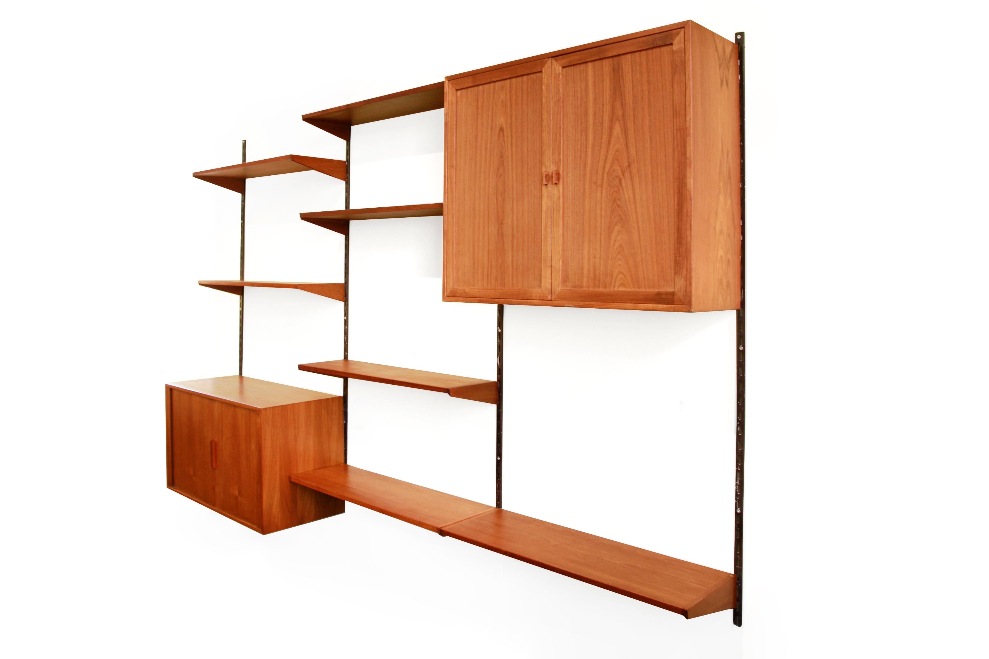 Mid-Century Modern Scandinavian teak wooden wall unit designed by Kai Kristiansen and produced by Feldballes Mobelfabrik, Denmark. Also known as FM Mobler. This shelving unit consists of 4 metal uprights, 7 shelves, a cupboard with two sliding