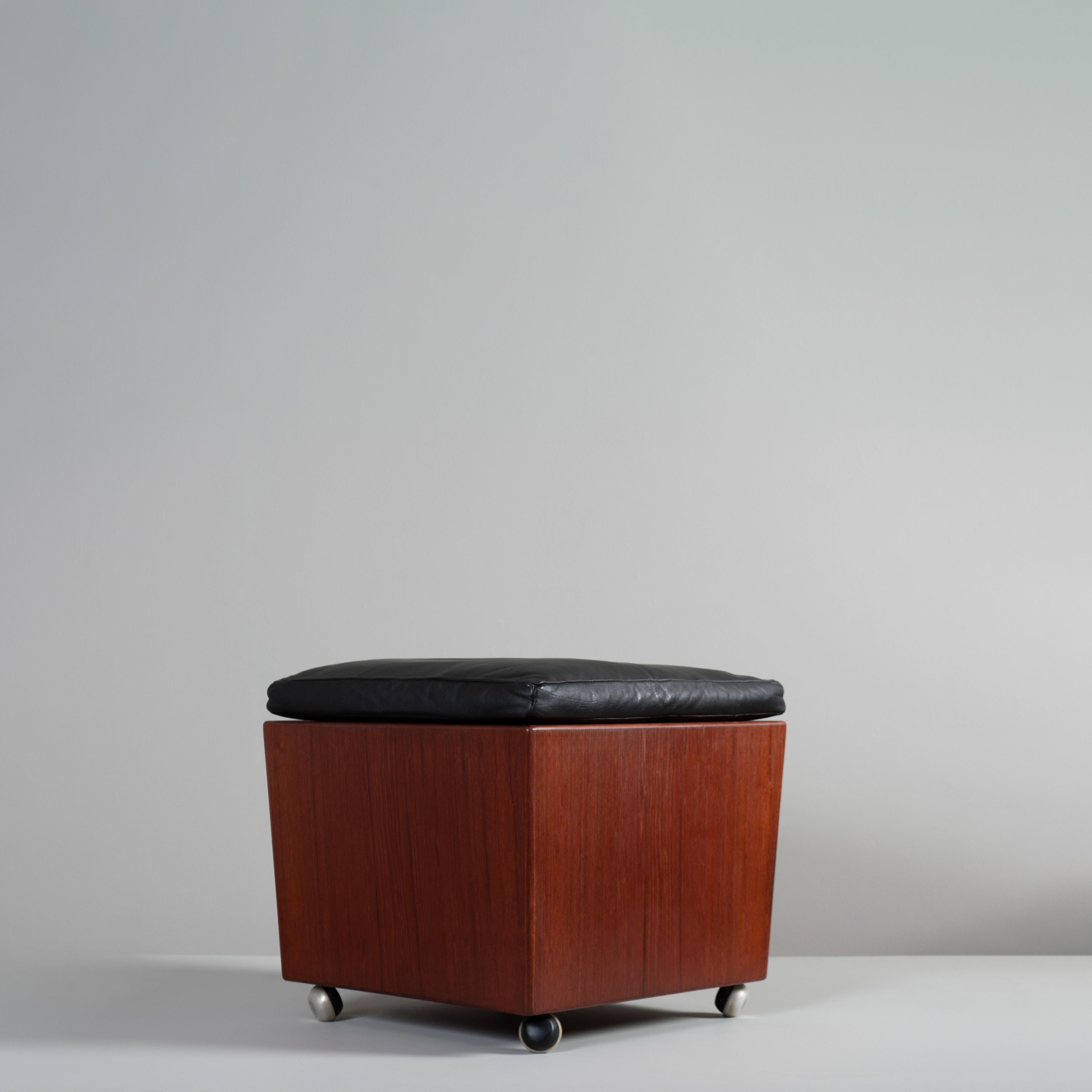 Un cubo portaoggetti su ruote in teak e pelle di altissima qualità. Il cuscino in morbida pelle si solleva dai suoi fissaggi per rivelare il coperchio con fori per le dita dell'area di stoccaggio all'interno. 
Si muove in modo estremamente fluido,