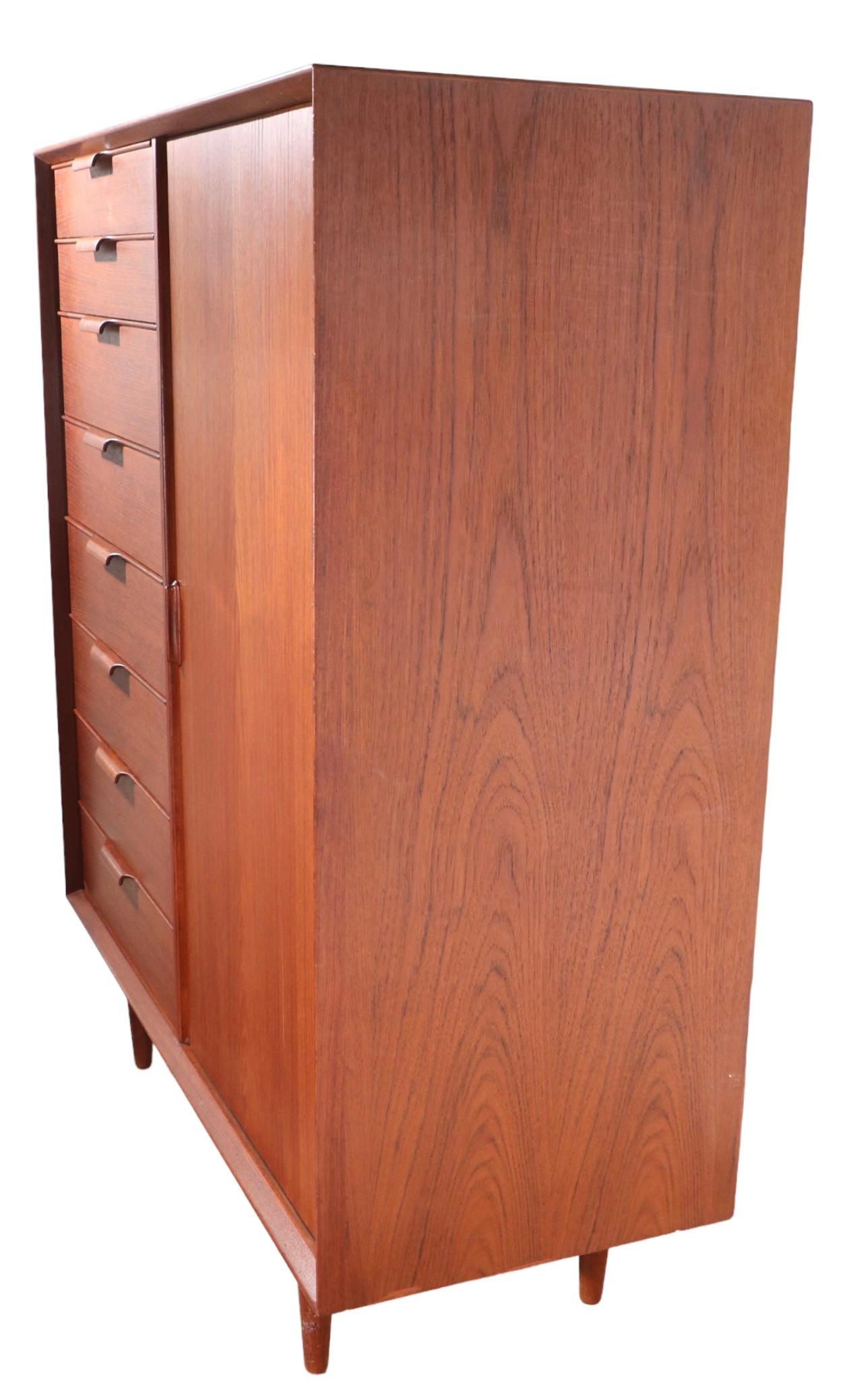 Stylish Danish Modern wardrobe made in Denmark by Falster Mobelfabrik. The chifferobe features a divided. cabinet with a bank of five drawers, flanked but a tambour roll door, that opens to an open closet to hang shirts, coats etc. This example is