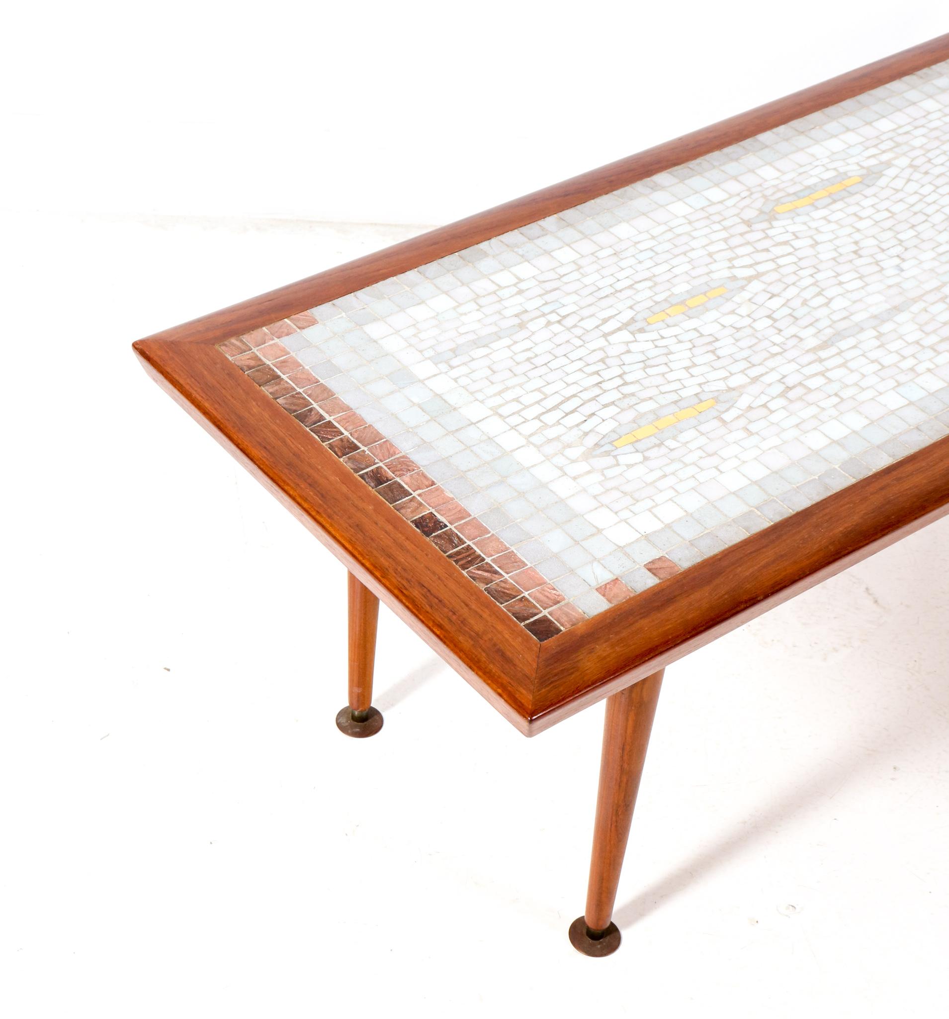 Amazing Mid-Century Modern coffee table.
Design by Berthold Muller.
Striking German design from the 1960s.
This amazing coffee table consists of four solid teak and brass legs with the original solid teak top inlaid with mosaic tiles.
This