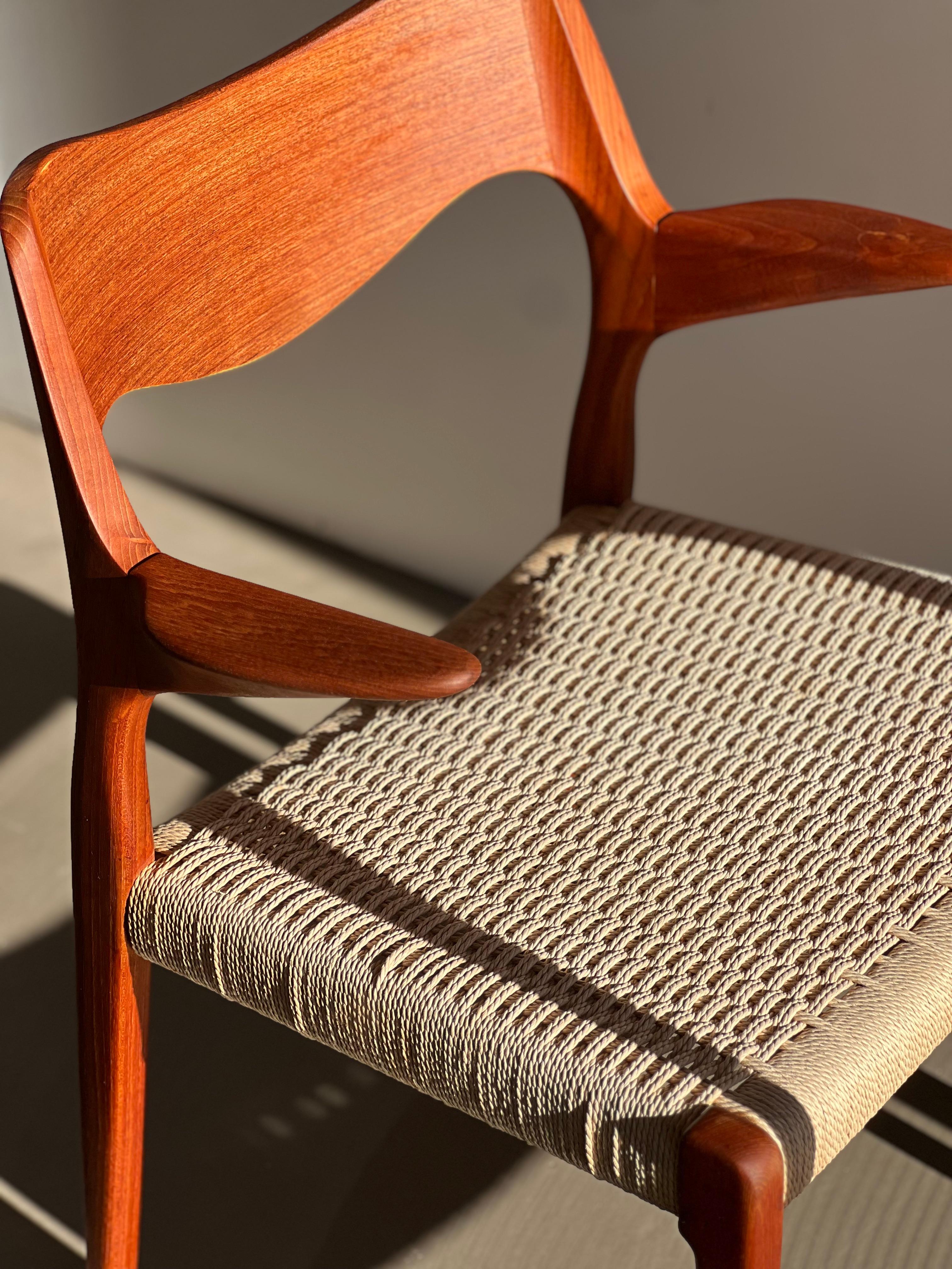 La chaise Møller Model 55, conçue par Niels Otto Møller dans les années 1950, est un chef-d'œuvre du design moderne danois. Dotée d'un cadre en bois massif sculpté, fabriqué en teck, et d'une assise en corde de papier tressée à la main, cette chaise