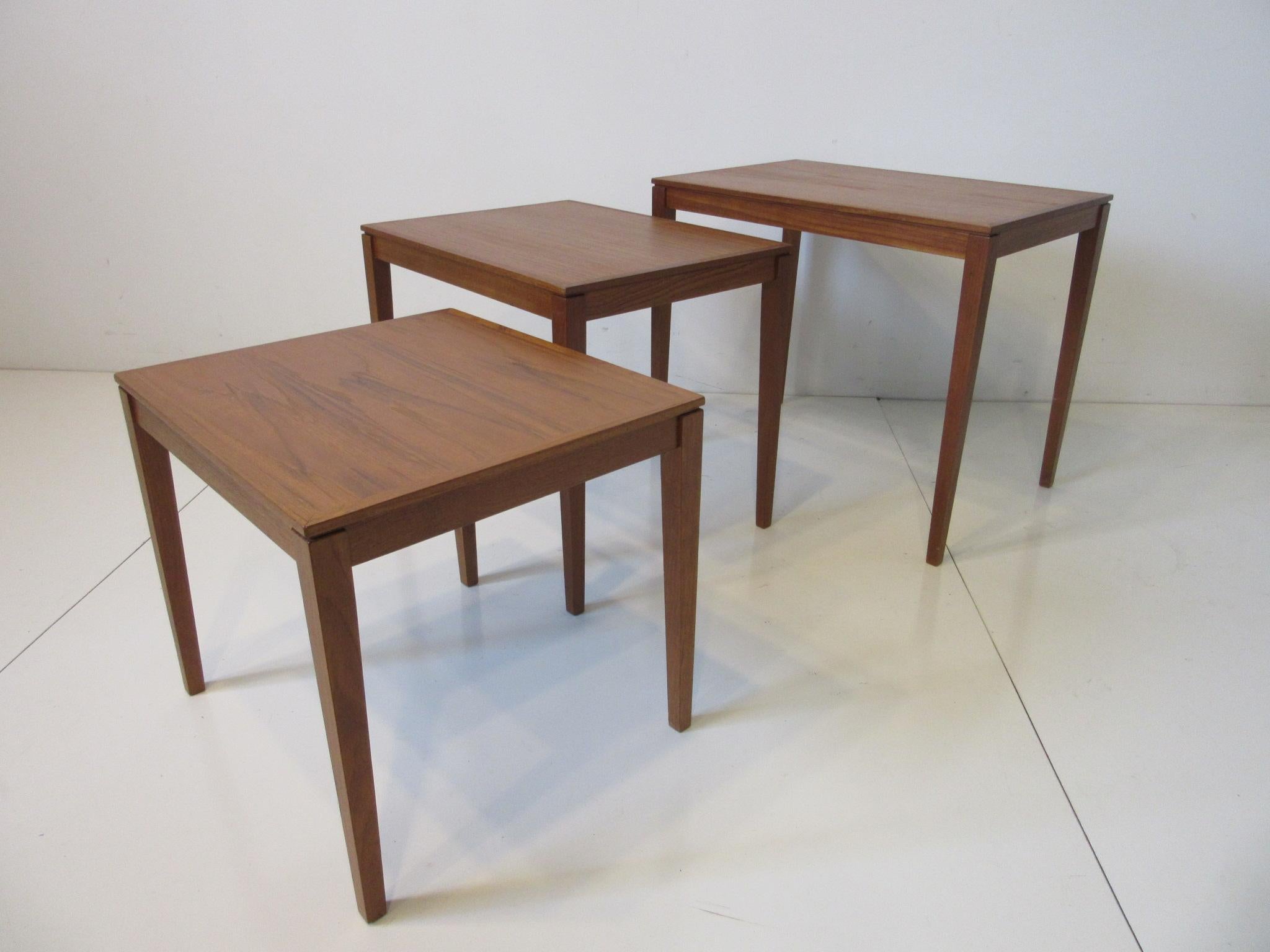 A set of three teak wood nesting side tables with wonderful graining and nice tapered side edges to the top retaining the manufactures branded marks to the bottoms by Bent Silberg Mobler made in Denmark.