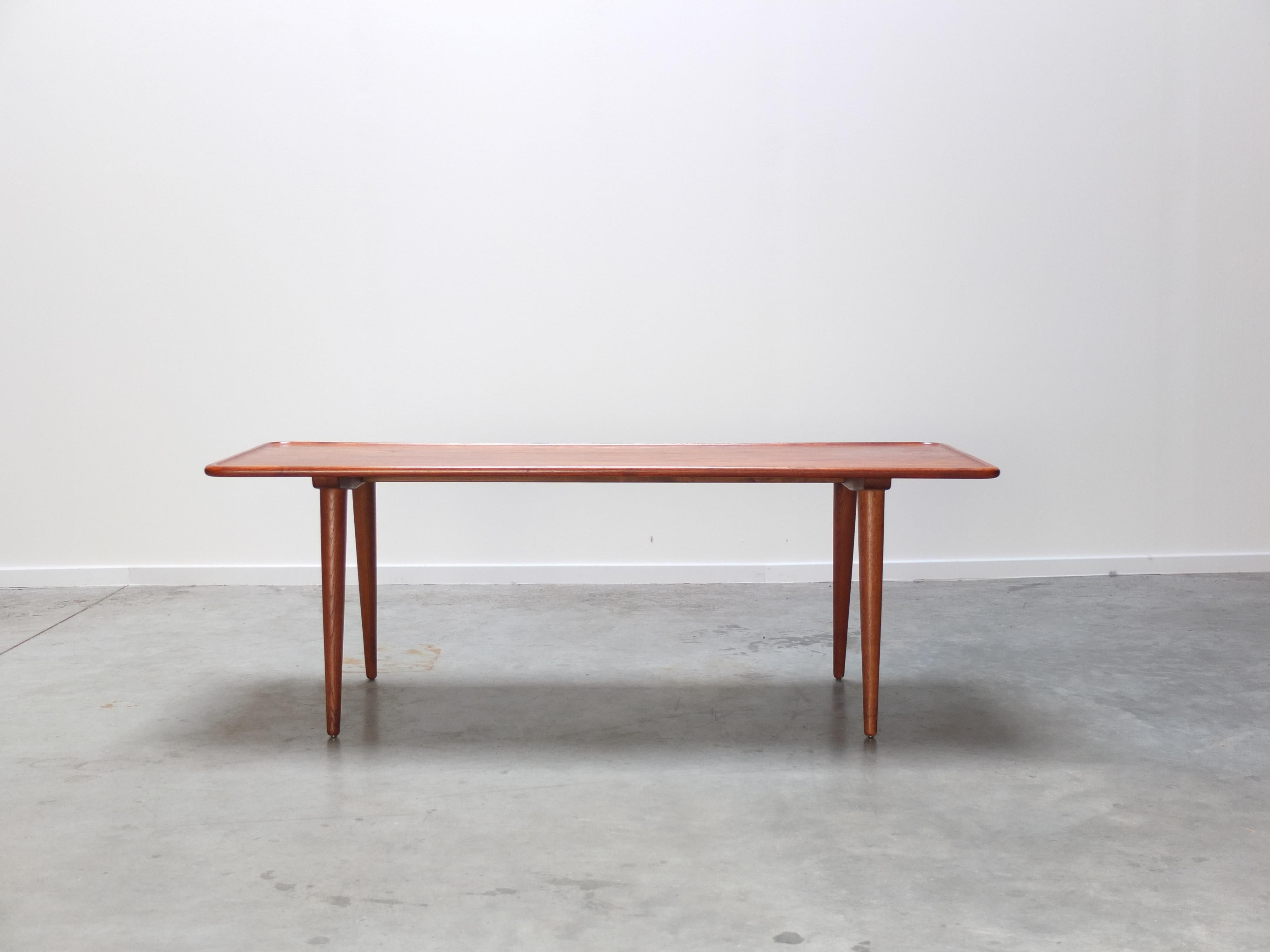 Lovely coffee table designed by Hans Wegner for Andreas Tuck in 1954. The top is made out of solid teak wood and stands and 4 oak tapering legs that spray at an angle. Great minimalist design with eye for detail such as the raised edge on the top.