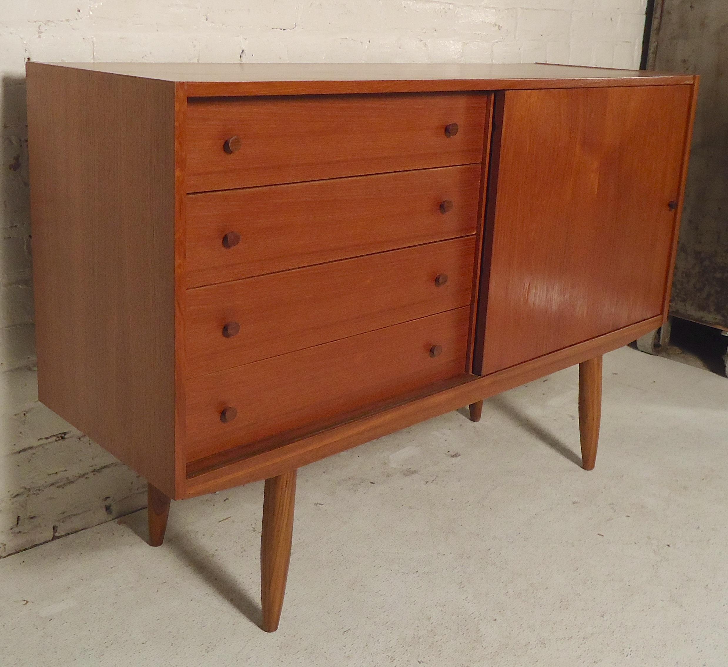 Mid-Century Modern teak cabinet with drawer storage. All teak wood grain with wood pulls and long tapered legs.

(Please confirm item location - NY or NJ - with dealer).
 