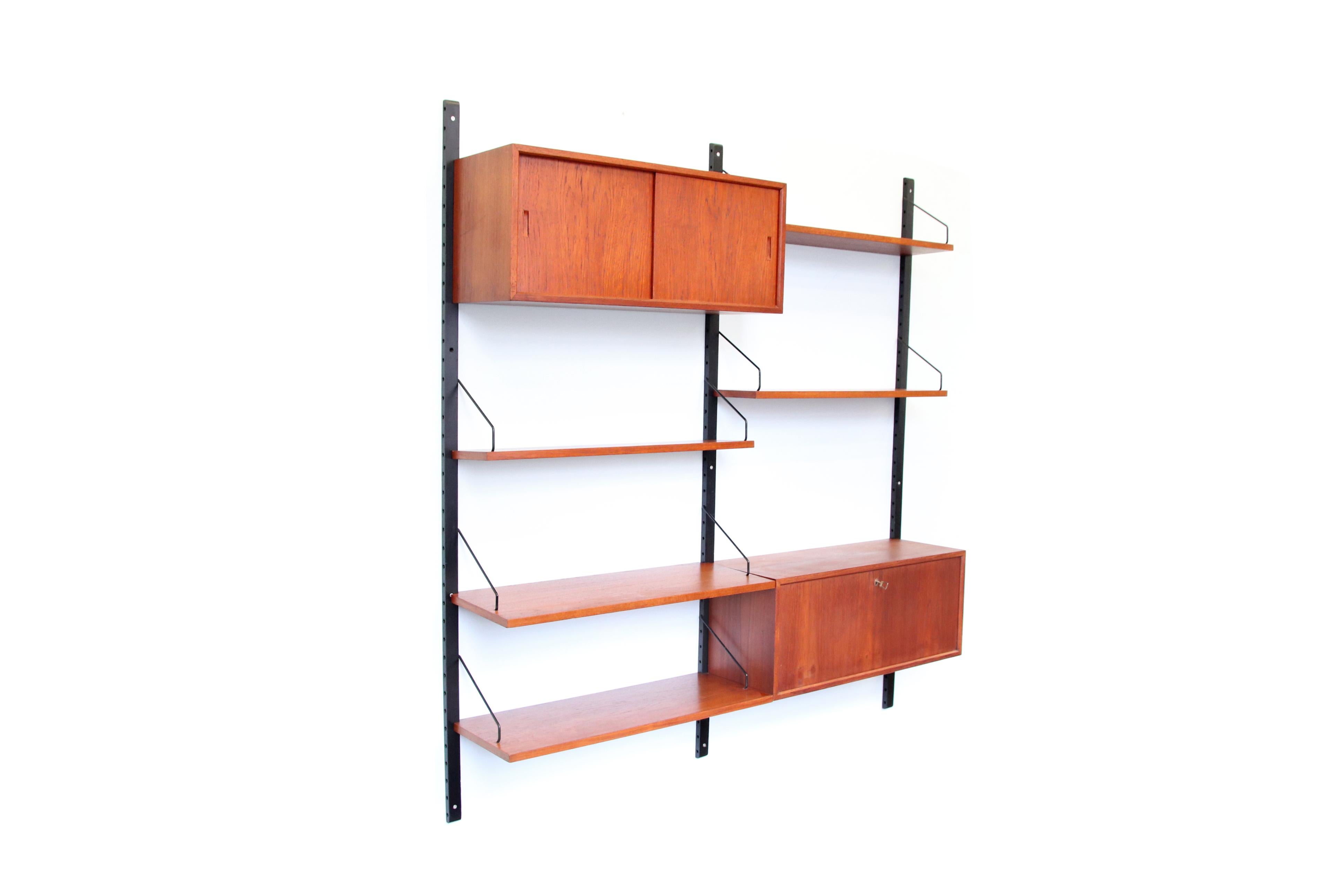 Teak wooden wall system designed by Poul Cadovius and produced by Royal System, Denmark. This wall cabinet from the 1960s consists of 3 black lacquered wooden uprights, 5 shelves, a cabinet with two sliding doors and a cabinet with a flap that can