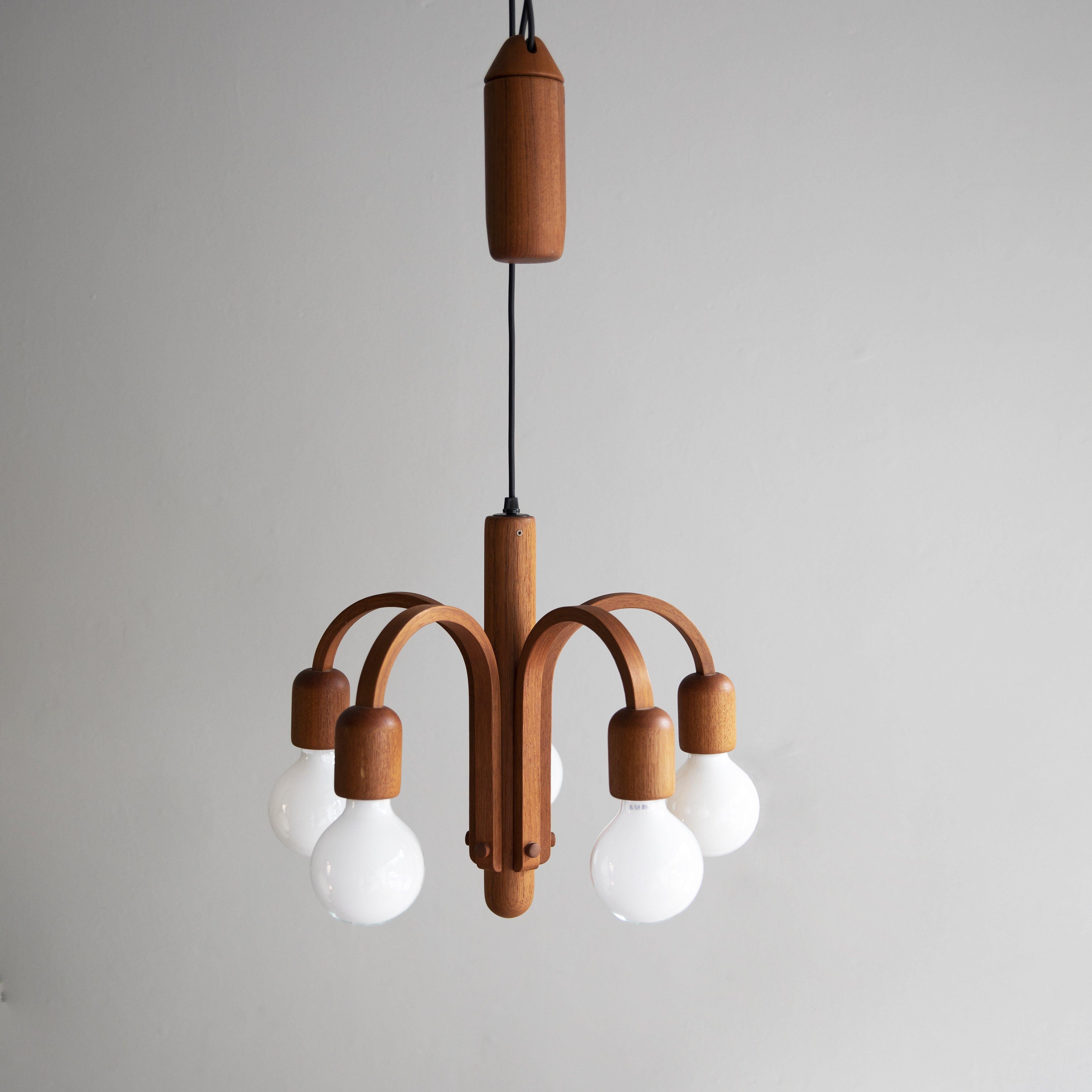 A five-arm rise ‘n’ fall chandelier in teak, most probably made in Germany, circa 1960. 
The centre of the light, from which the five arms extend, is a solid piece of teak carved into a torpedo shape. Echoing this are the bulb holders and the