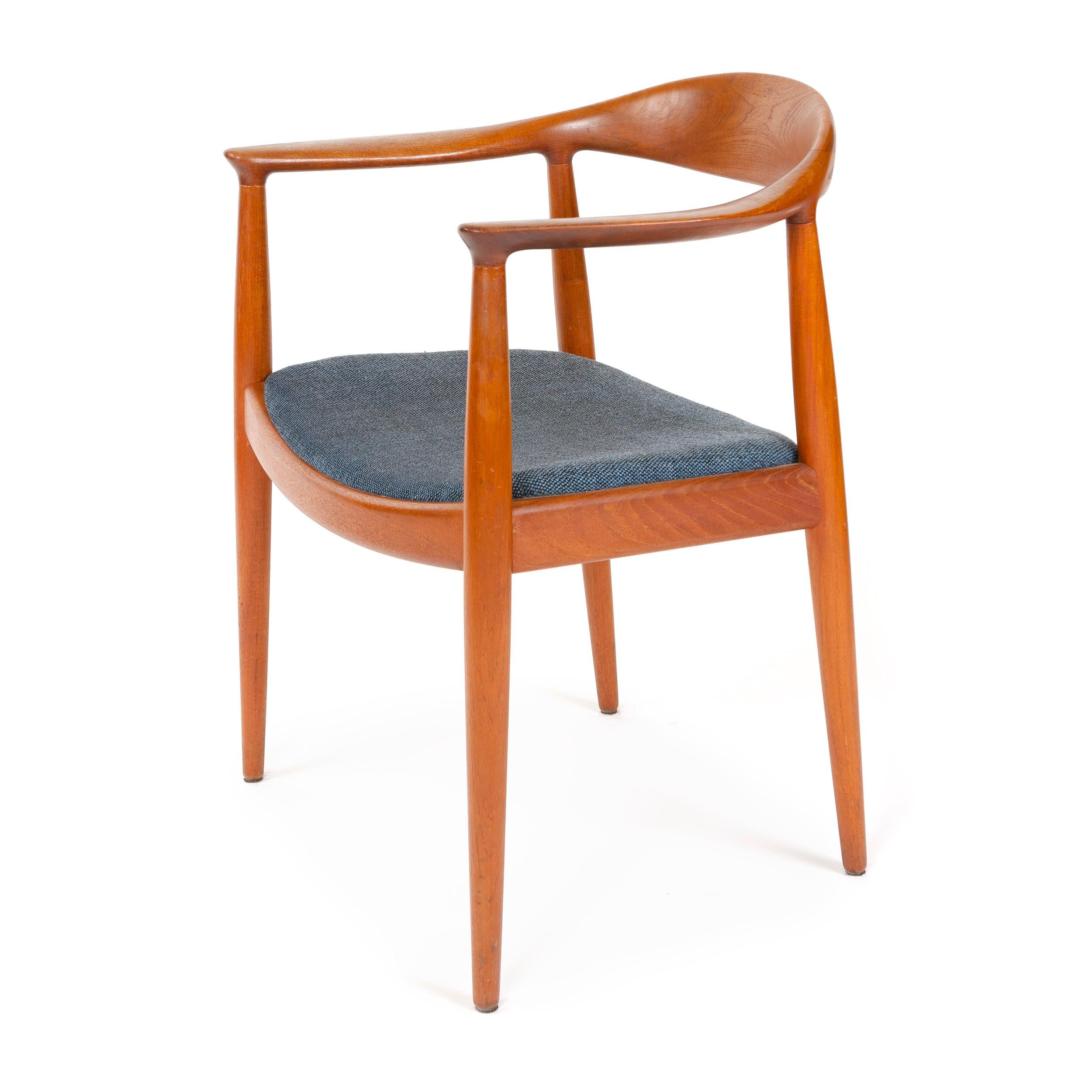 A teak Scandinavian Modern 'Round' chair by Hans Wegner. This armchair / dining chair features a masterfully sculpted backrest and arms floating atop tapered dowel legs and an upholstered seat. Designed by Wegner in 1949, made by Johannes Hansen in
