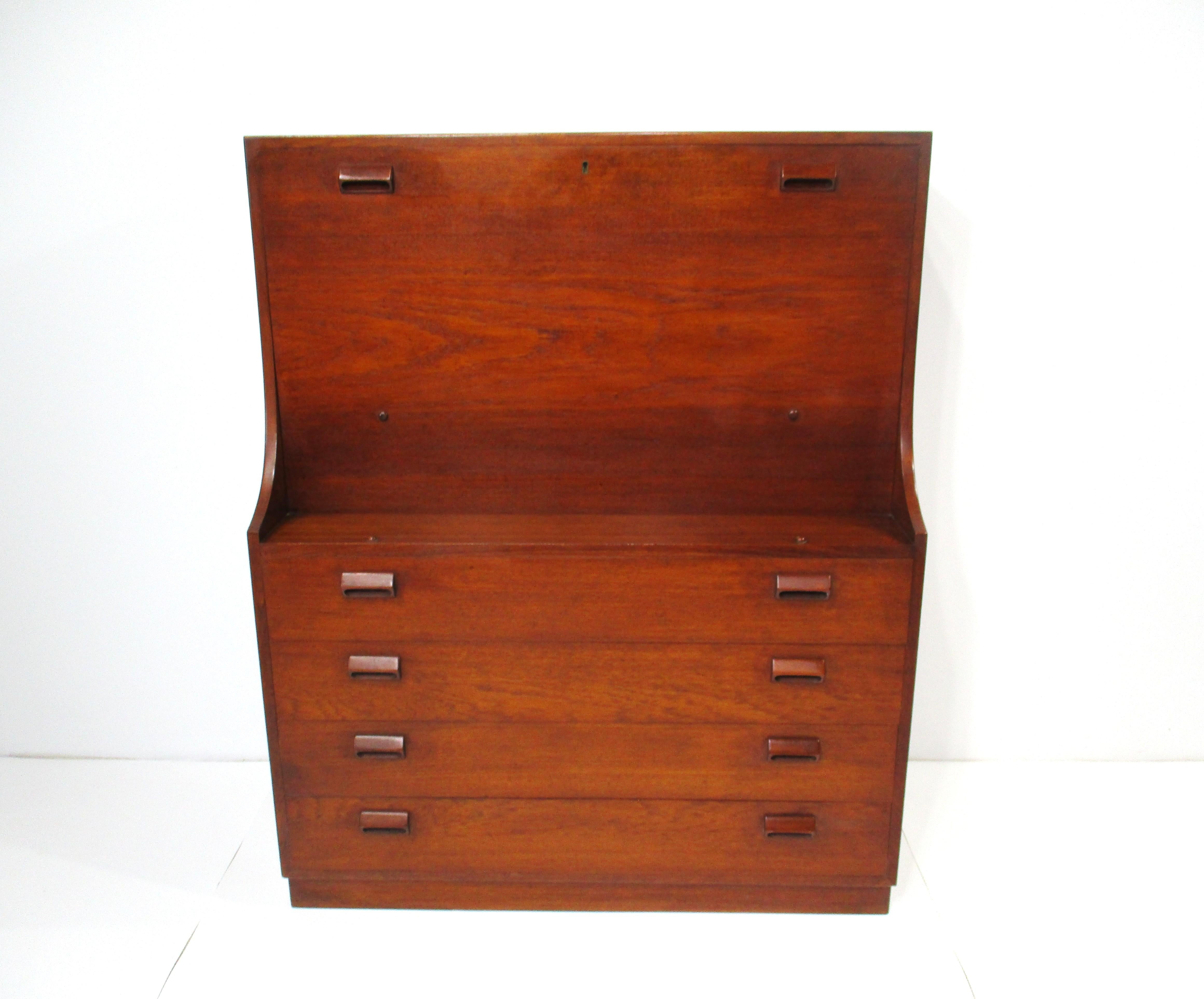 Una cassettiera per segretaria in legno di teak molto ben progettata, con quattro cassetti inferiori e la parte anteriore che si ripiega come piano della scrivania rivelando vani portaoggetti sulla destra e due cassetti sull'altro lato. I cassetti