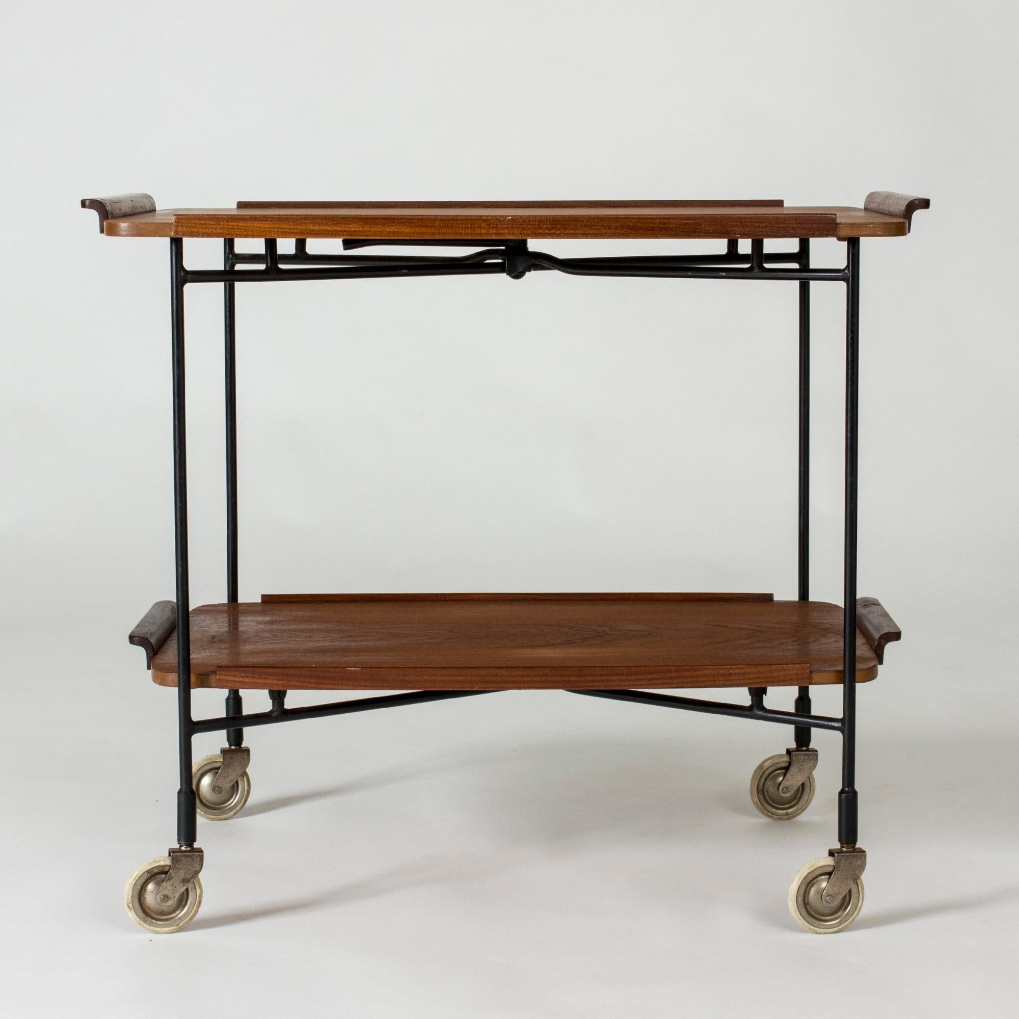 Very cool serving cart from Firma Glas & Trä, made from black lacquered metal and teak. The two teak trays can be lifted off and the cart folded. Elegant details.