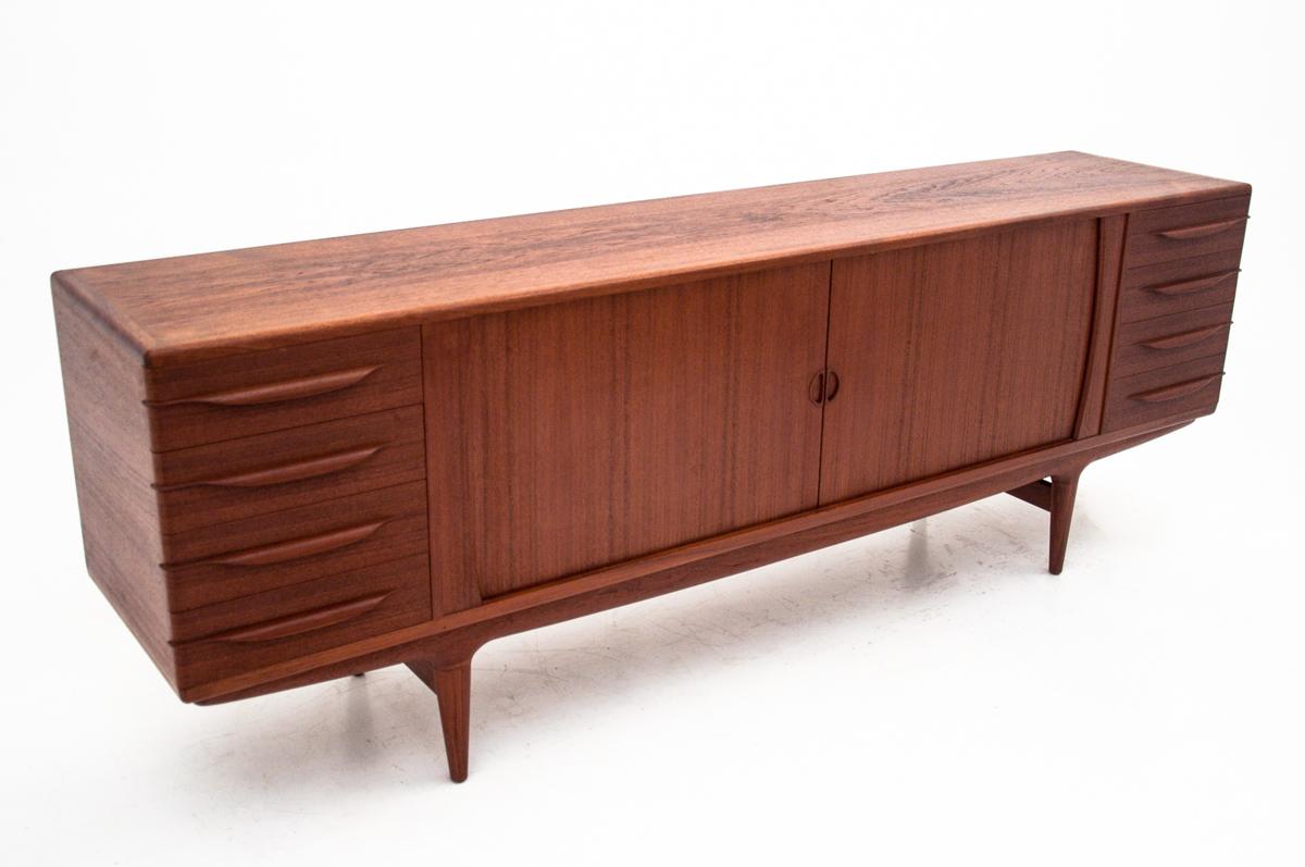 Long Danish teak sideboard with drawers and sliding doors comes from Denmark from the 1960s.
It was designed by the Danish designer Johannes Andersen for Uldum Mobelfabrik.
It has four drawers in each of the corners, and behind the sliding shutter