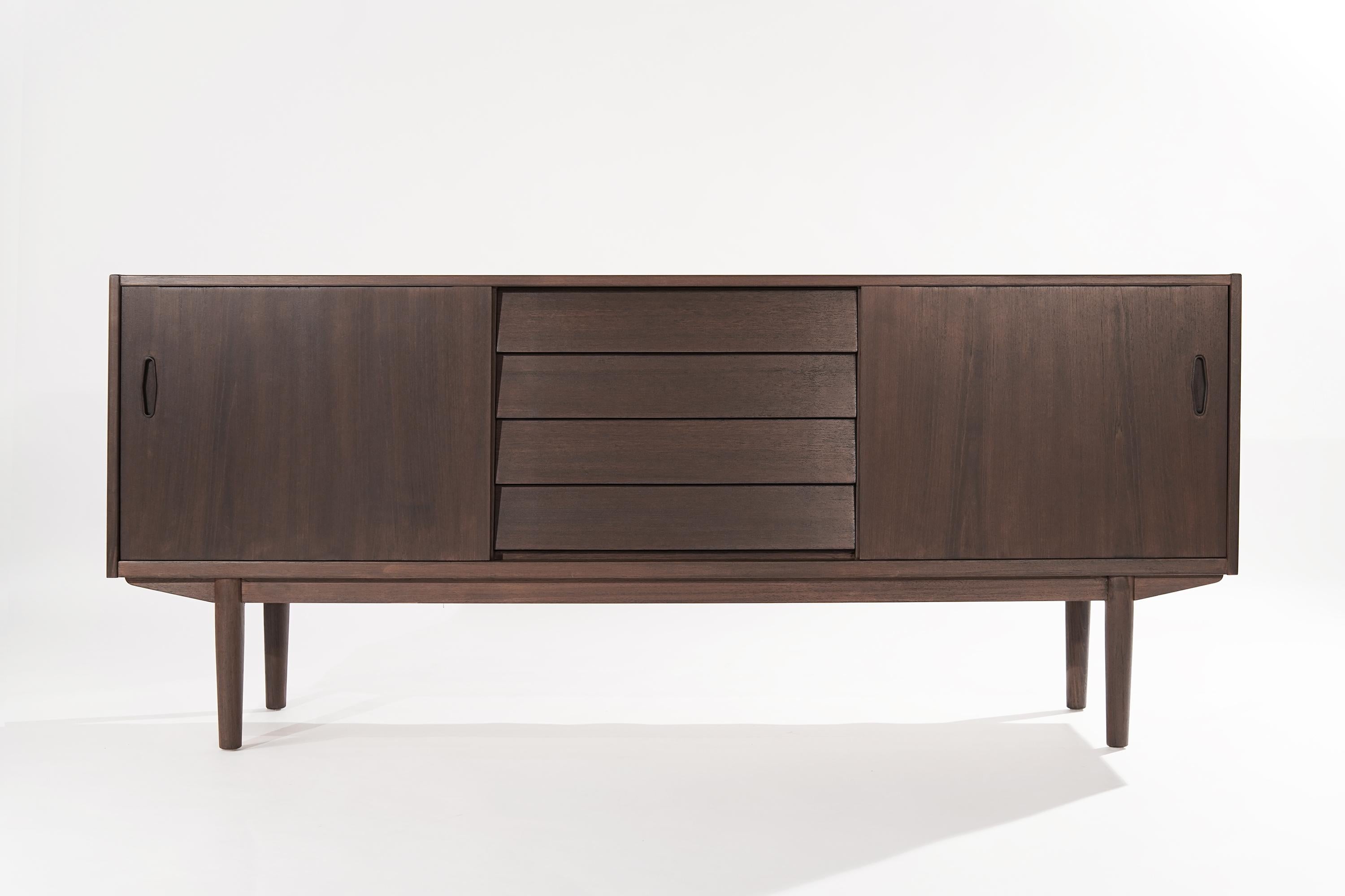 Teak sideboard or credenza designed by Nils Jonsson for Hugo Troeds, Denmark, circa 1950-1959.

Completely restored, featuring four center drawers, the top drawers offers slotted silverware storage. The sliding doors open up to reveal single