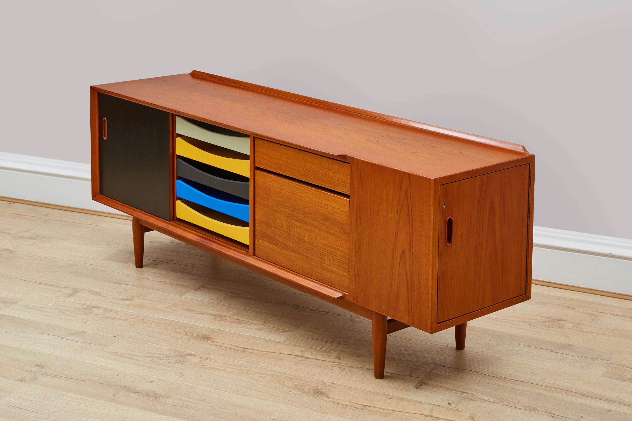 Teak wood with painted draws Credenza sideboard. Four drawers of different colours, a box and a sliding door opening onto a storage with an adjustable shelf. The door flips over and has one side painted black and the other teak. On the right side