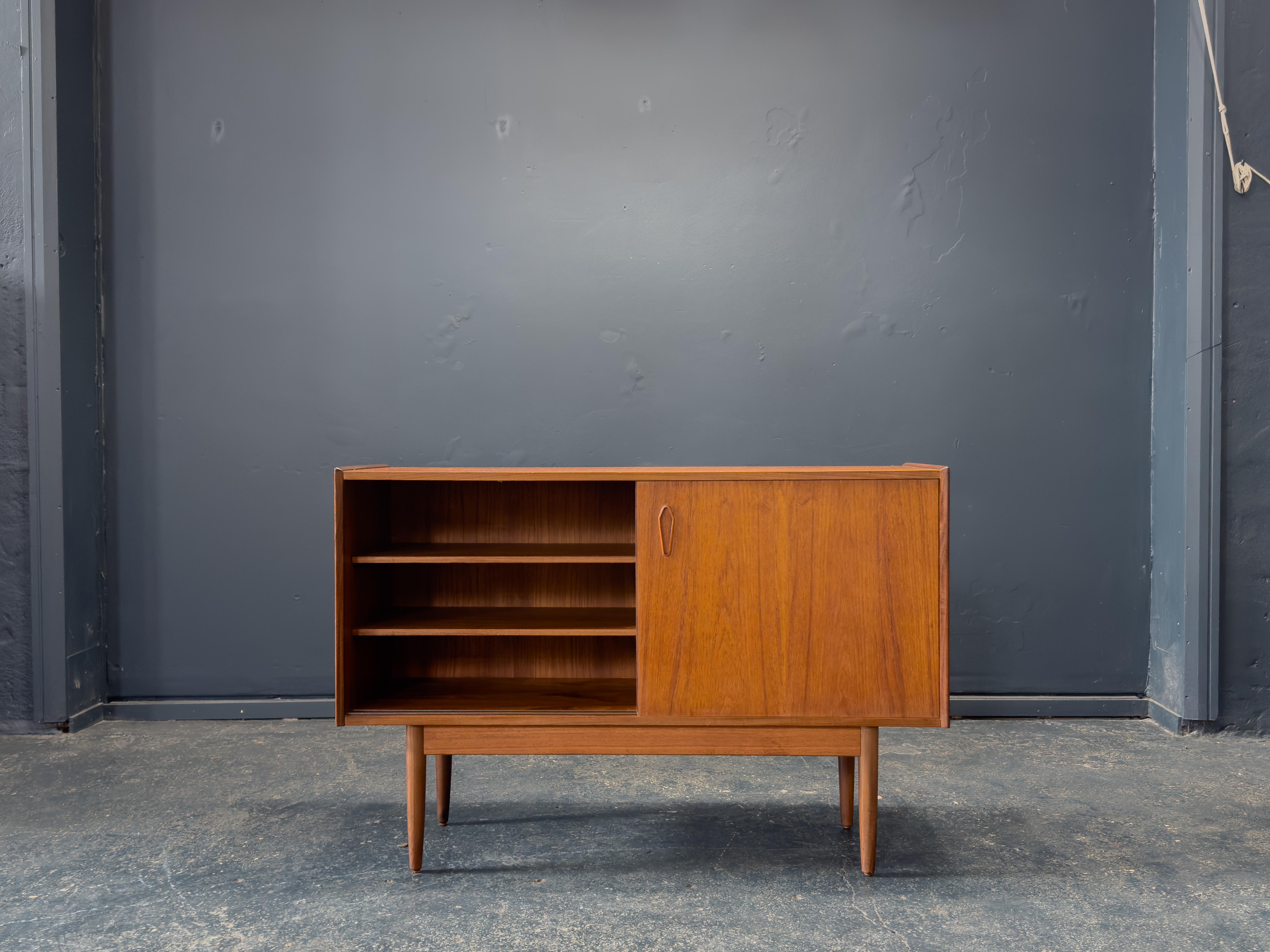 Questa elegante credenza in teak è un raffinato esempio di design nordico di metà secolo, che offre sia calore visivo che spazio funzionale. Realizzato in teak con una bella venatura, le sue linee pulite e il suo profilo minimalista riflettono i