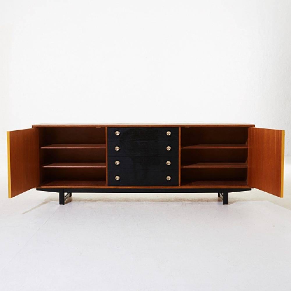 Sideboard 1950, teak veneered, partially painted, brass buttons.
Height about 65, 180 × 44 cm.
The key can be recovered, minor superficial damage.
