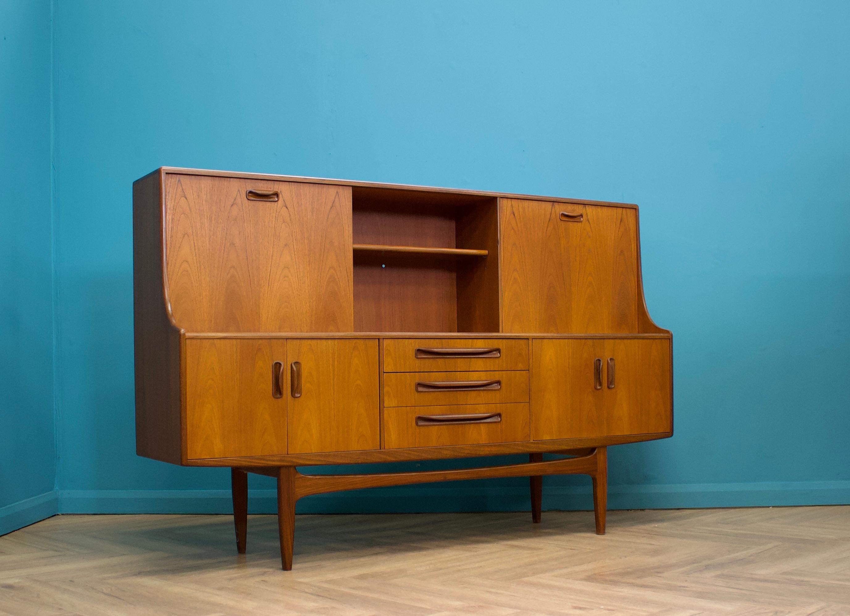 - Mid century modern highboard or sideboard.
- Featuring a pull down drinks cabinet and a sliding cupboard door.
to the top.
- Manufactured by G Plan in the UK.
- Made from teak and teak veneer.