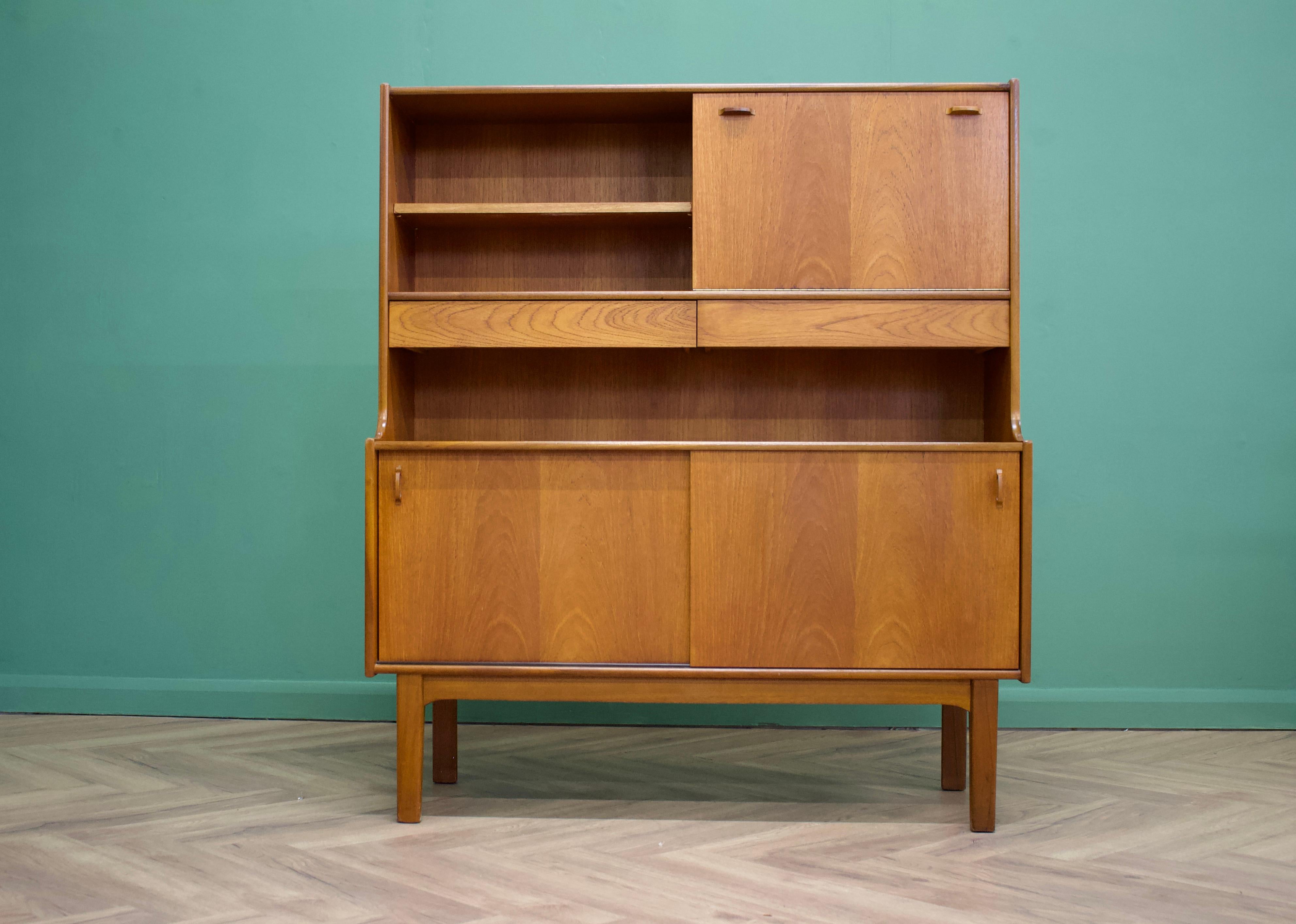 - Mid century modern highboard or sideboard
- Featuring a pull down drinks cabinet, two sliding door cupboards, two drawers and a shelf
- Manufactured by Nahan in the UK
- Made from teak and teak veneer.