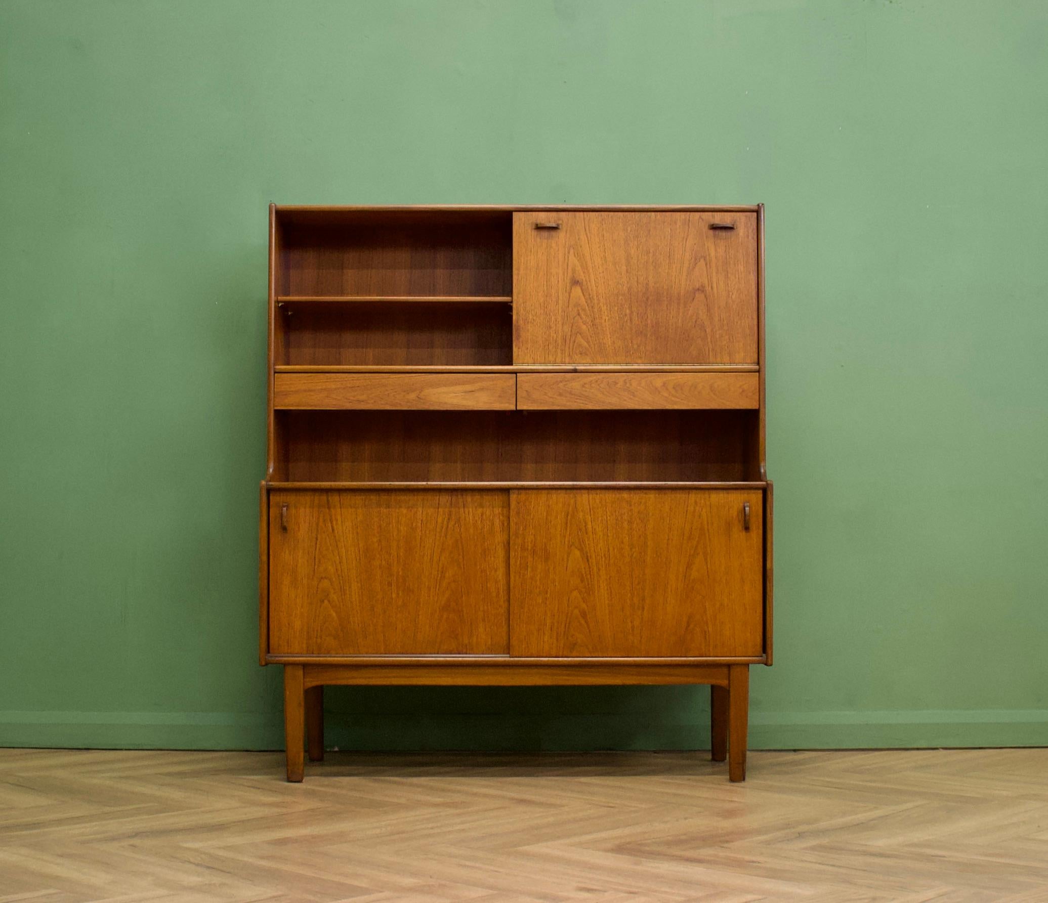 - Mid century modern highboard or sideboard
- Featuring a pull down drinks cabinet, two sliding door cupboards, two drawers and a shelf
- Manufactured by Nahan in the UK
- Made from teak and teak veneer.