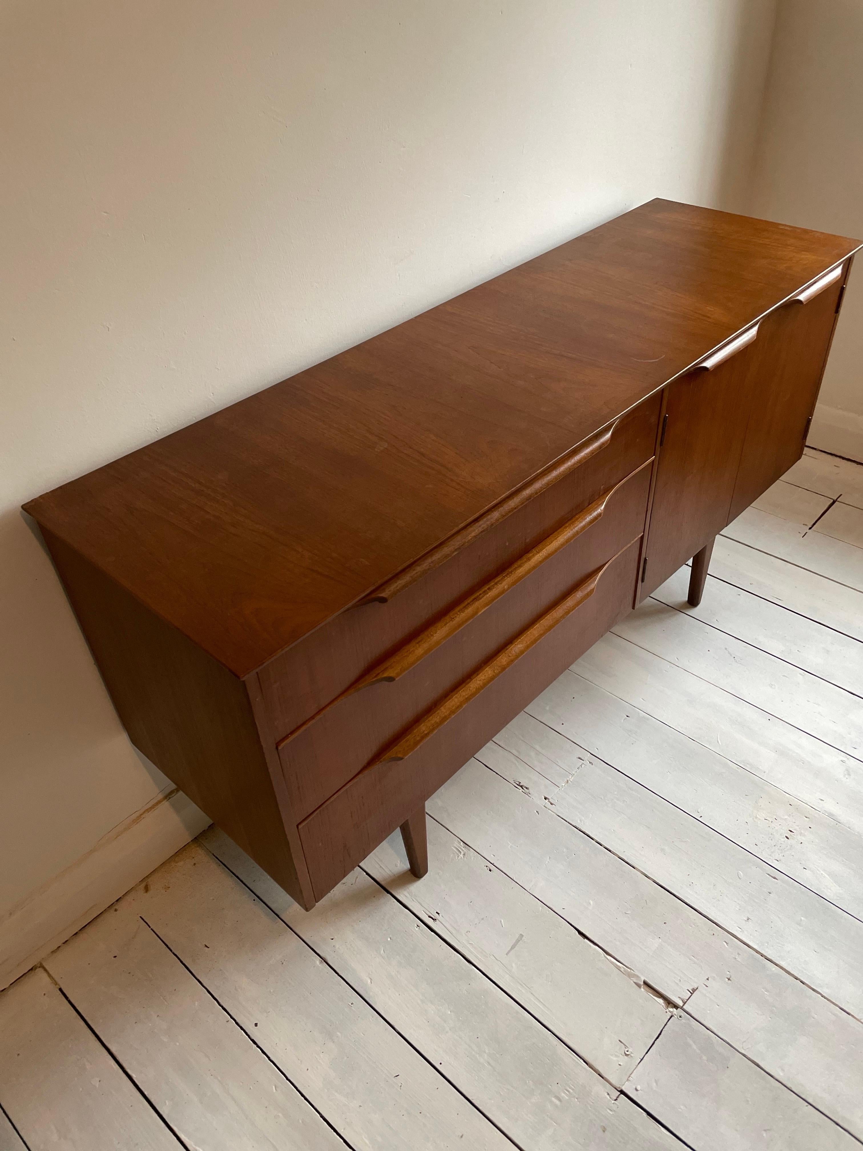 A beautifully designed & crafted 1960s teak sideboard manufactured by Stonehill Furniture.

Featuring teak handles, two shelved cupboards. The teak has a lovely vintage golden patina that only age can achieve.

There is also a bank of three drawers.