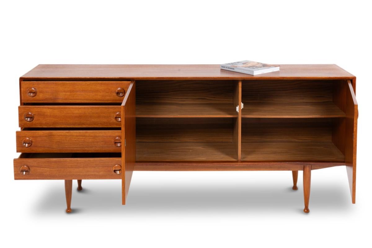 Rectangular teak sideboard, opening on the front with four drawers on the left side and two doors, with shelves inside. Spindle-shaped base ending in balls. Circular, openwork handles.

Work realized in the 20th century.

Dimensions: H 86 x W 200 x