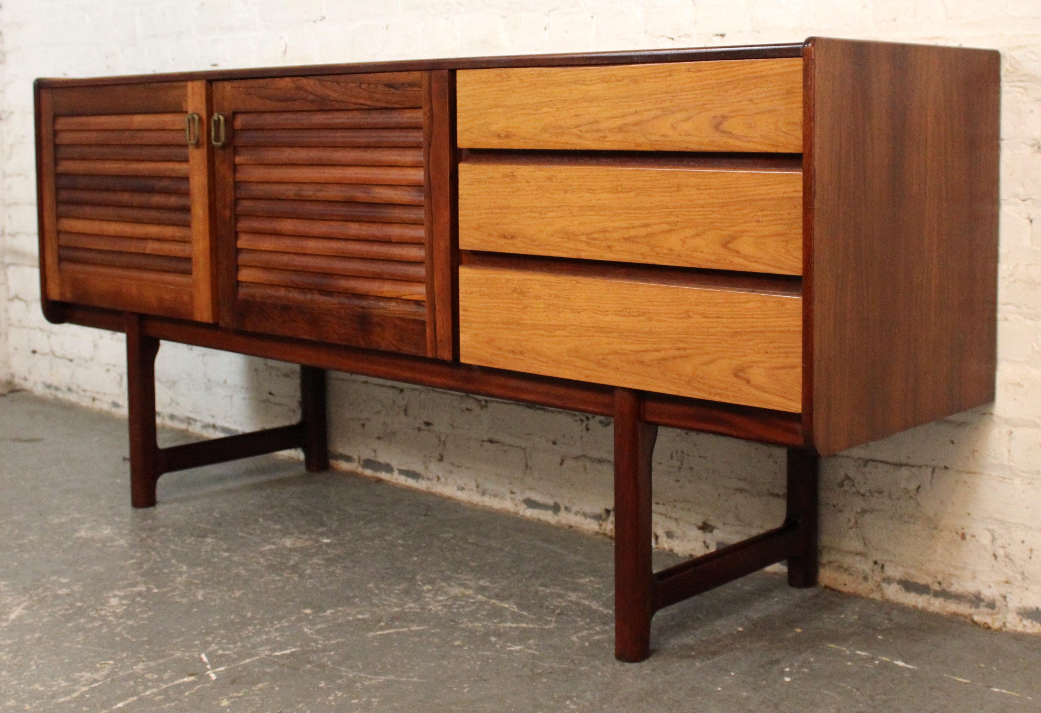 A striking Mid-Century Modern teak sideboard designed by A. H. McIntosh of Kirkcaldy, Scotland. This beautifully crafted piece features distinctive louvered cabinet doors, contrasting tones of warm teak and lighter oak-faced drawers, and elegant