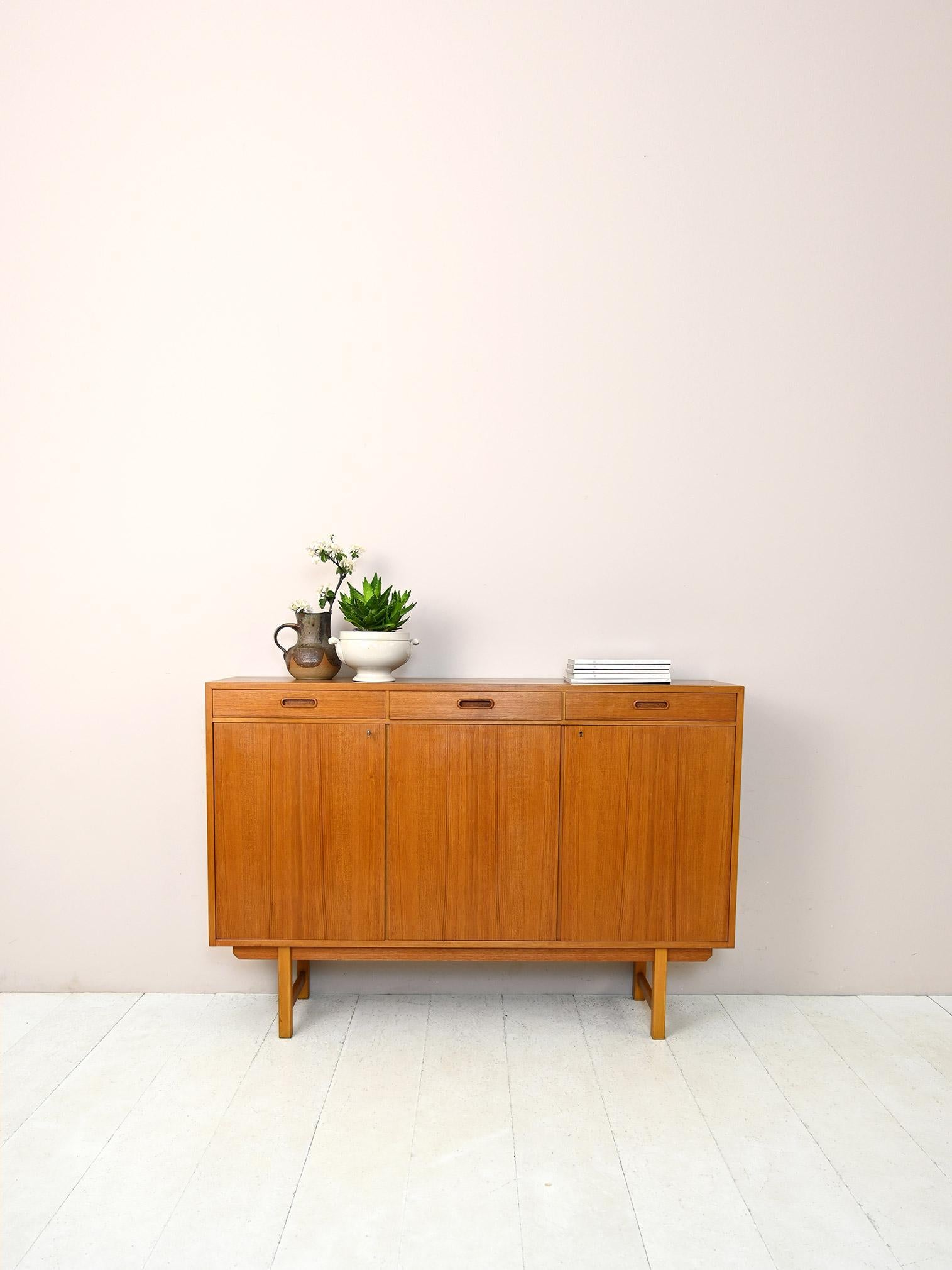 Scandinavian vintage 1960s sideboard.

A modern piece of furniture with square, minimalist lines. The frame features three convenient drawers with a carved wooden handle and three hinged doors equipped with a lock. Internally, it is divided into
