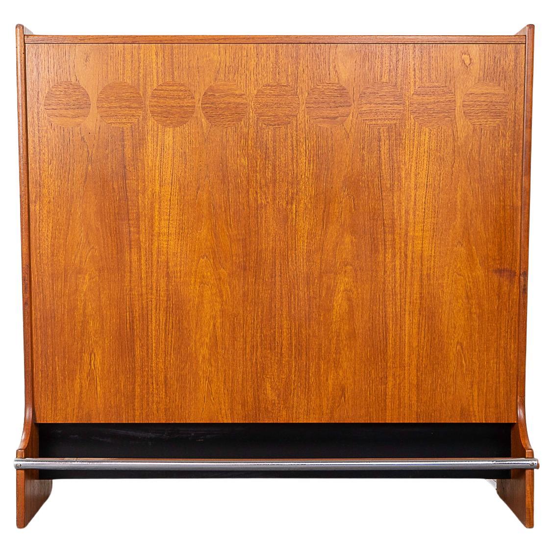 Teak Danish cocktail bar by Johannes Andersen for Skaaning & son, circa 1960's. Very handsome freestanding design with beautiful cross grained elliptical marquetry, sculpted door pulls and a chromed steel foot rest. Upper section flips & drops open