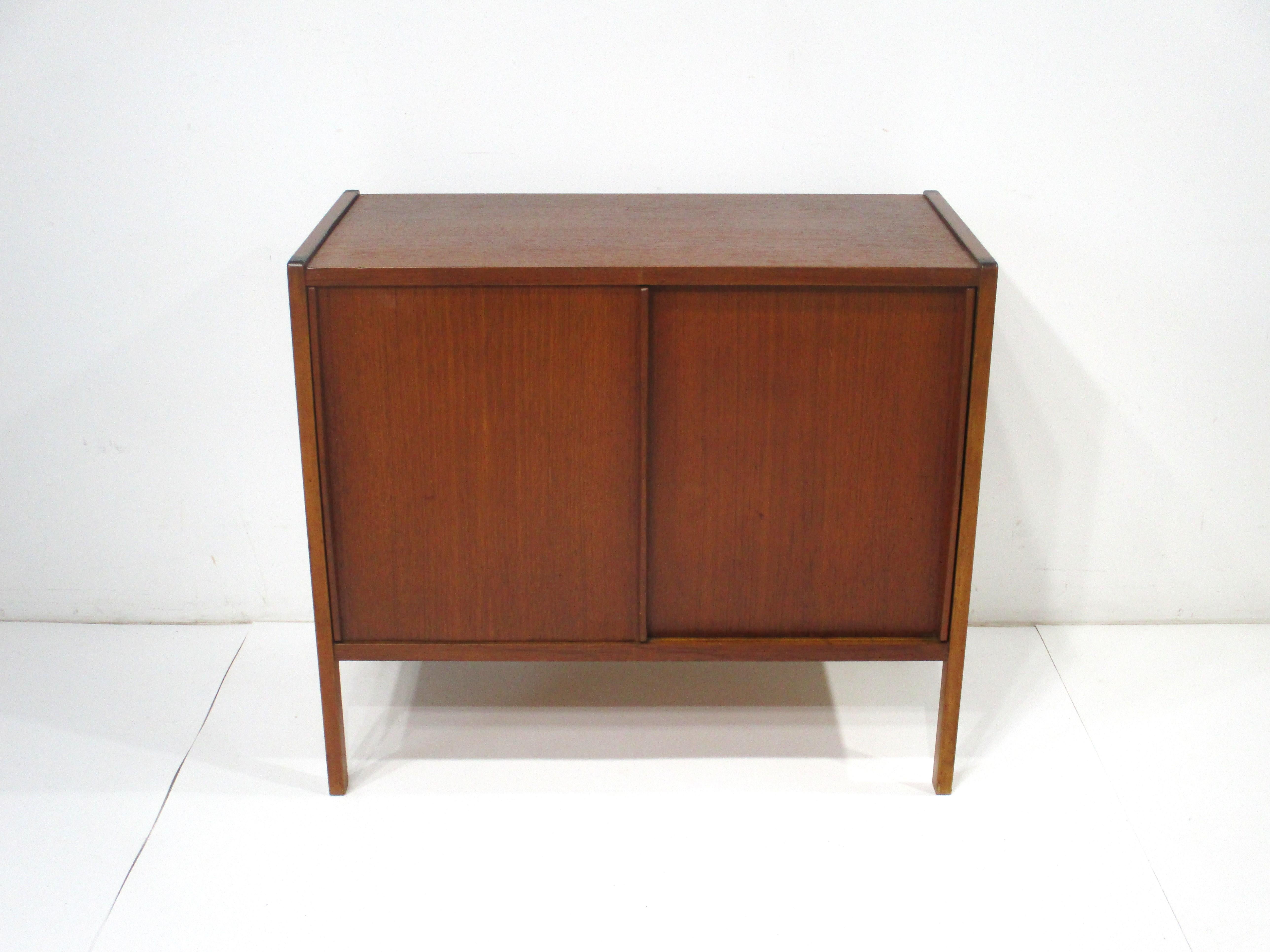 A smaller scale teak wood cabinet / credenza with double sliding doors having great long pulls . Inside a contrasting birch wood interior with one non adjustable shelve and a finished teak back . The perfect piece for a tight  
 space or that hard