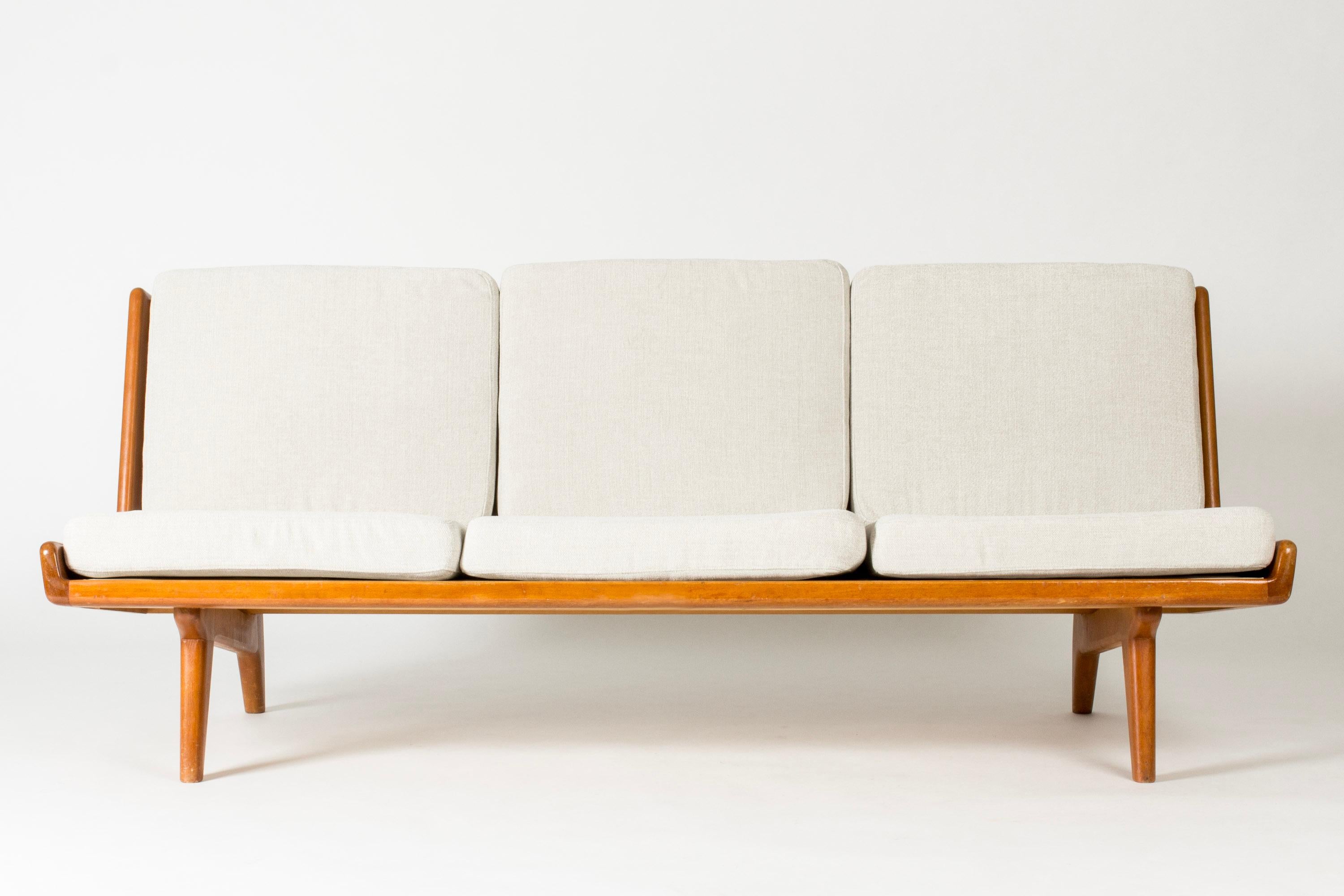 Divano di Gustaf Hiort af Ornäs, realizzato in teak con dettagli scultorei. L'incredibile schienale in pelle con fettuccia rende questo divano un vero e proprio gioiello della stanza. Seduta rivestita in tessuto color crema.