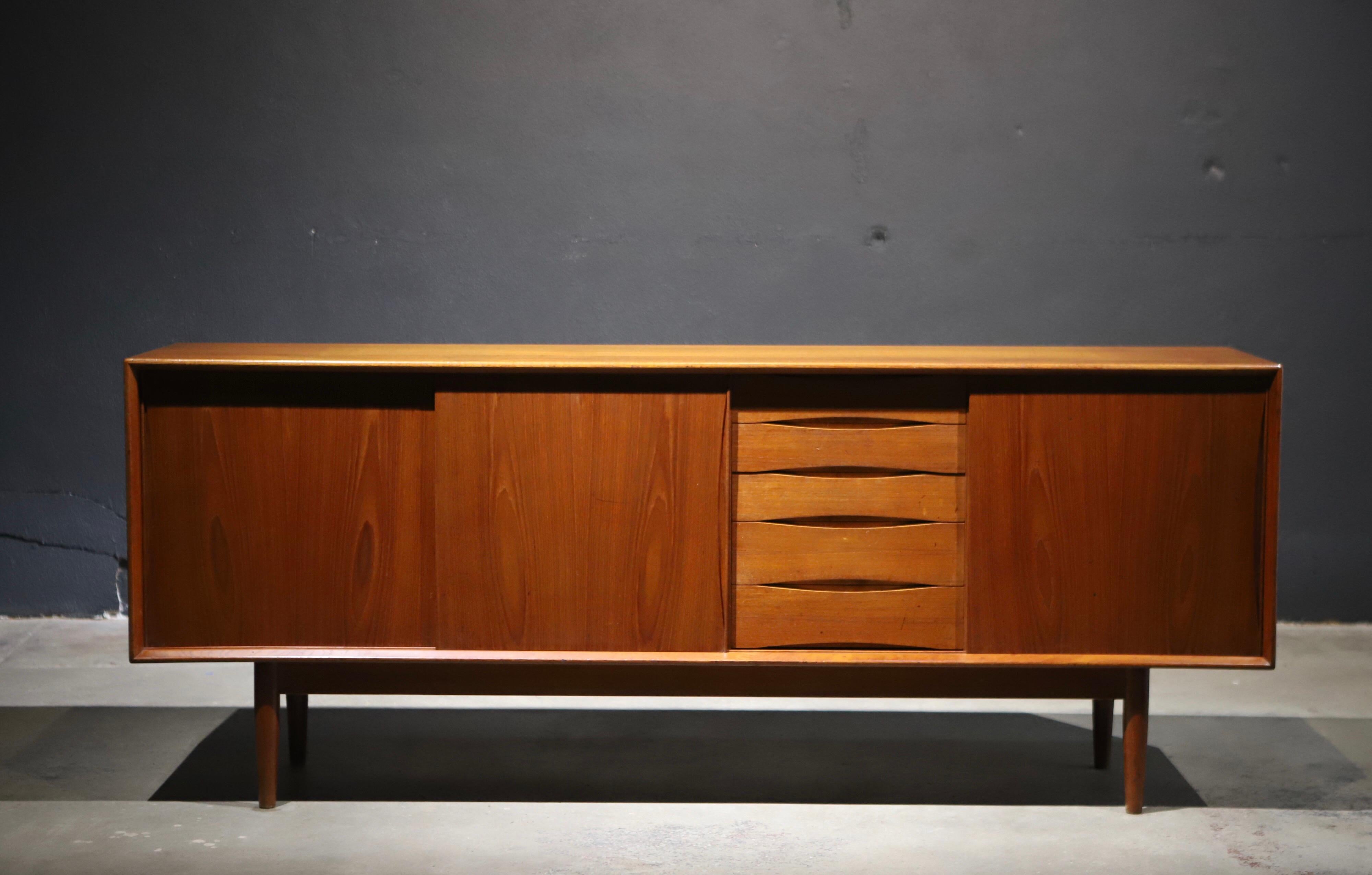 Beautiful teak credenza or sideboard with three sliding doors, one large storage area, one smaller and five drawers. A stunning piece with similar lines to well known Danish architect Finn Juhl. Stamped made in Sweden. Photographed with Eames wire