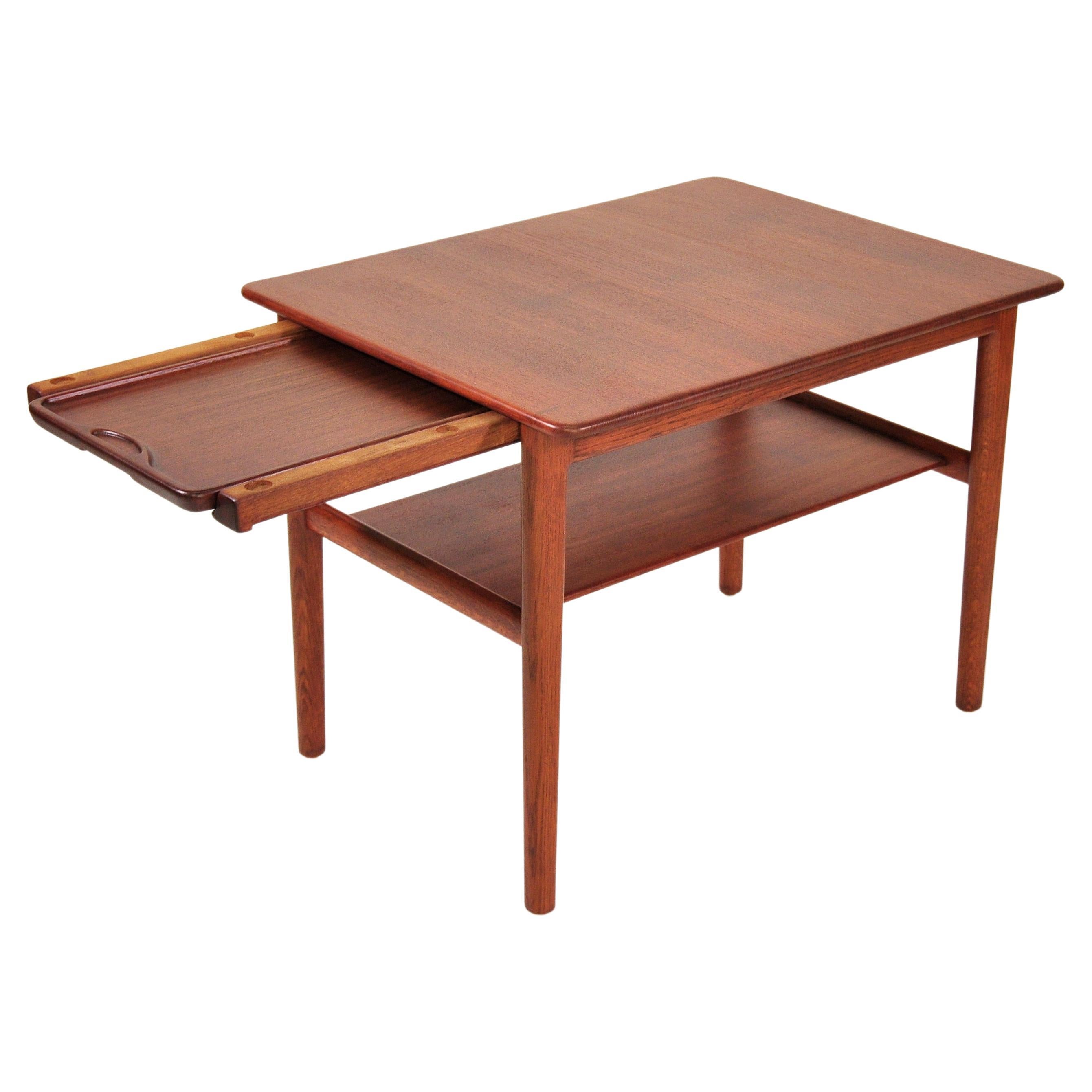 A very rare two-tier teak and oak occasional table with hidden tray, designed by Hans Wegner for Johannes Hansen. The end table features a two-tiered design with a solid teak top and shelf, oak legs and spanners, and a pull-out serving teak tray.