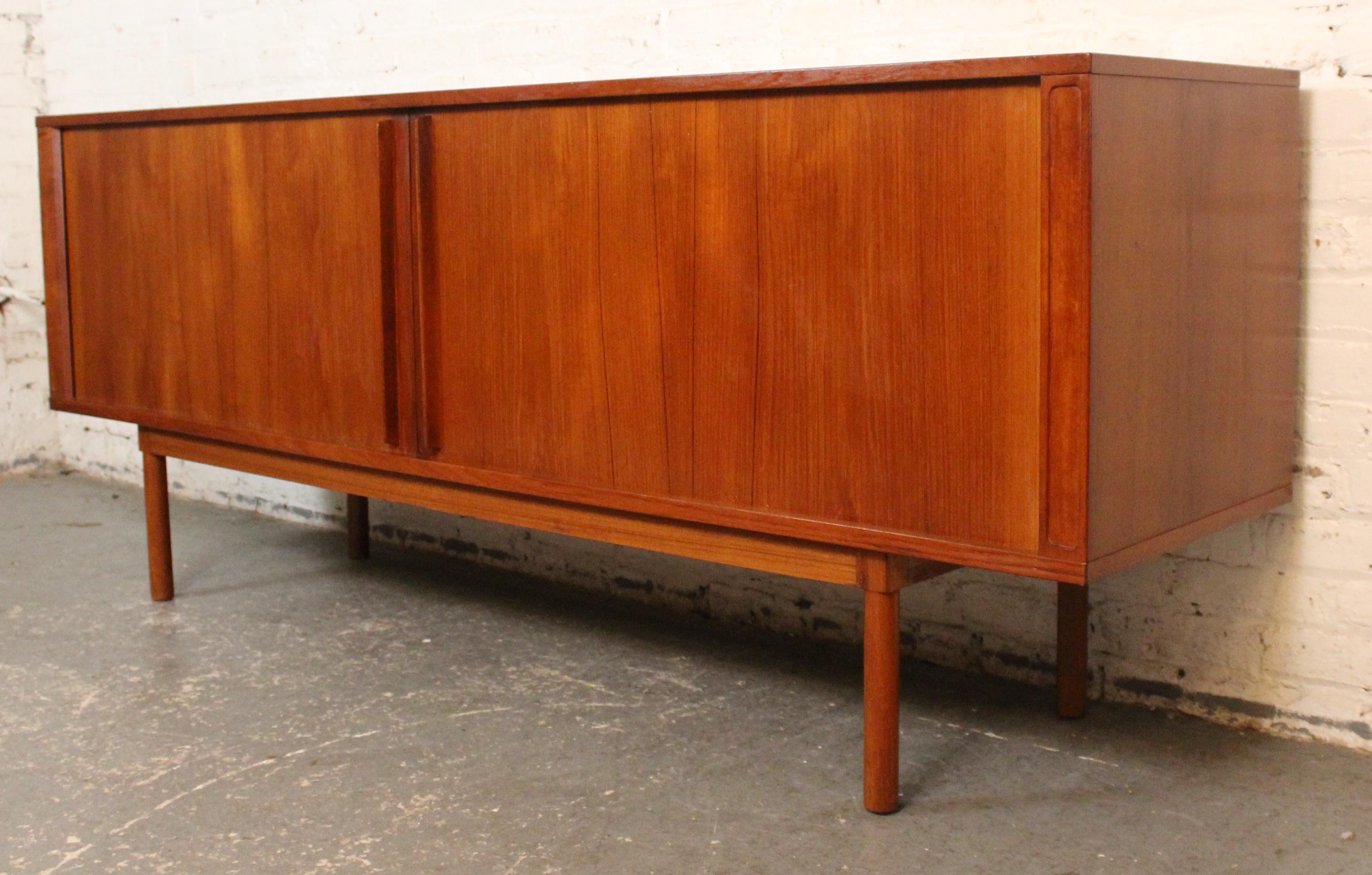 Esempio di design moderno danese, questa credenza vintage in teak di Jens Quistgaard per Lovig Dansks è caratterizzata da ante a tamburo di ottima fattura che scorrono agevolmente dietro il mobile per rivelare scaffali e cassetti regolabili. Con le