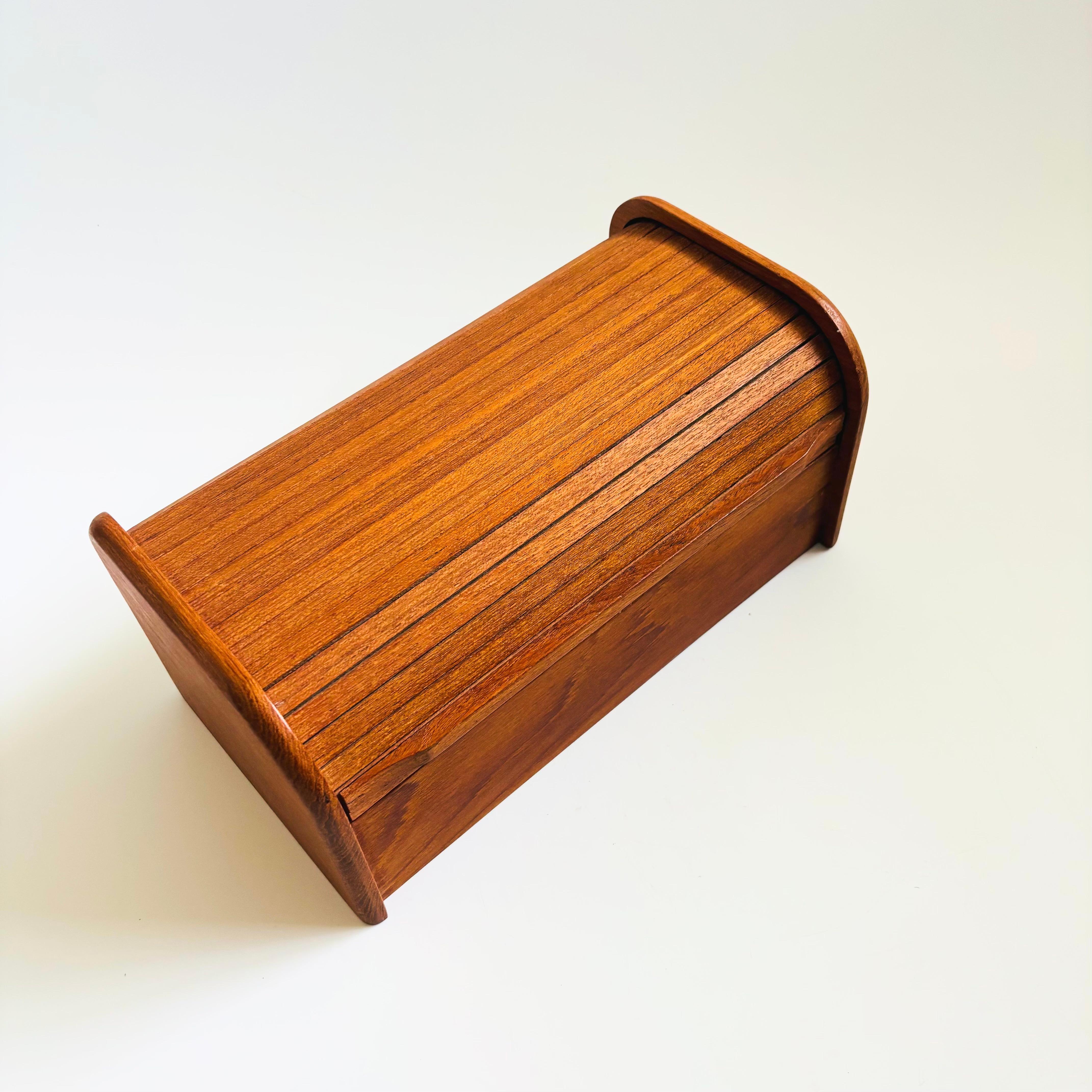 Una scatola portaoggetti vintage con ante a tamburo in teak. Ha un coperchio a tamburo che si apre per rivelare un ampio scomparto. Un unico divisorio in legno attraversa il centro. Un'elegante scatola per tenere le cose più strane lontano da occhi
