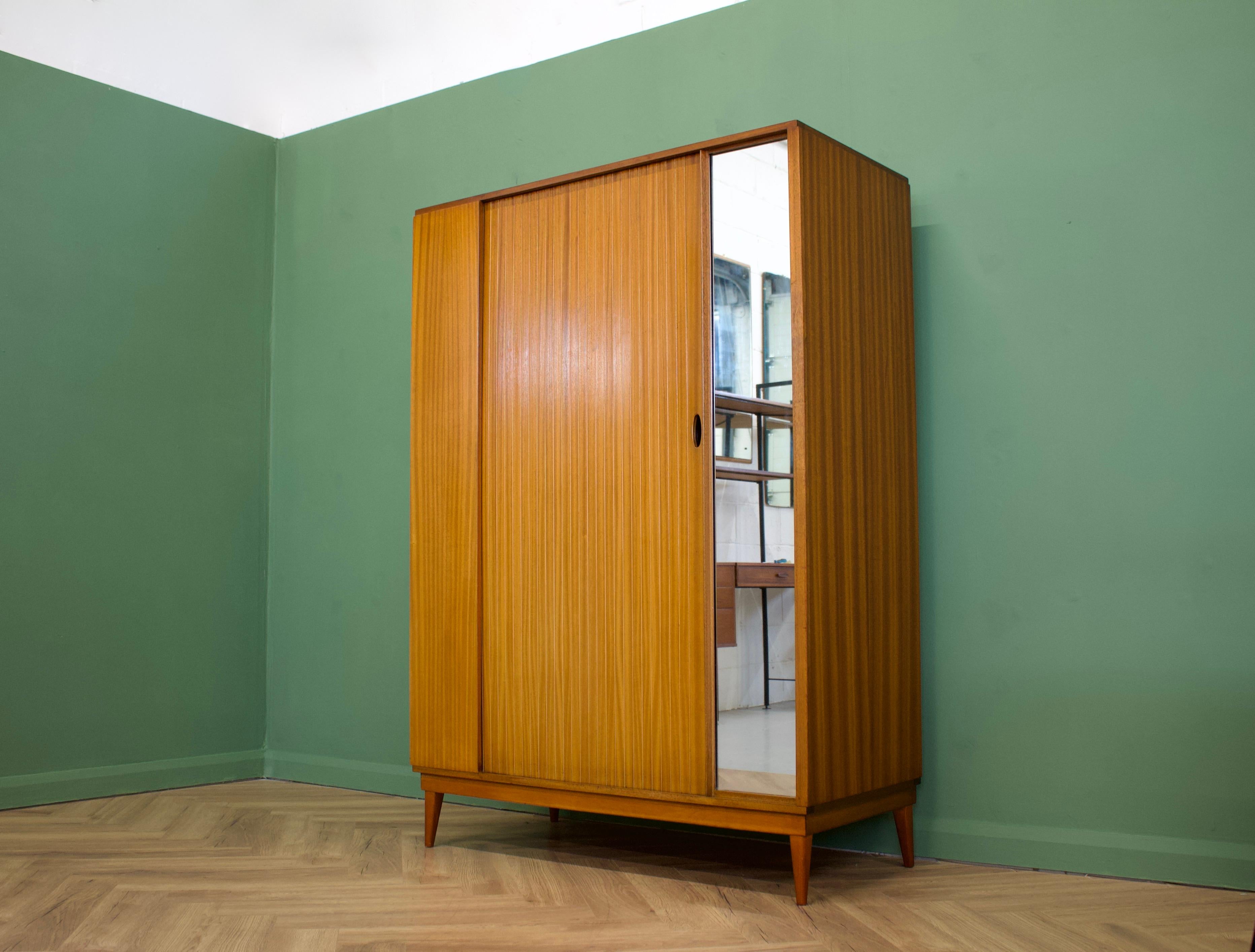 - Mid-Century Modern wardrobe.
- Manufactured by Austinsuite in the UK.
- Made from teak and teak veneer.
- Featuring a tambour door and a rail the full width.
- Also features a full length mirror to to the outside.