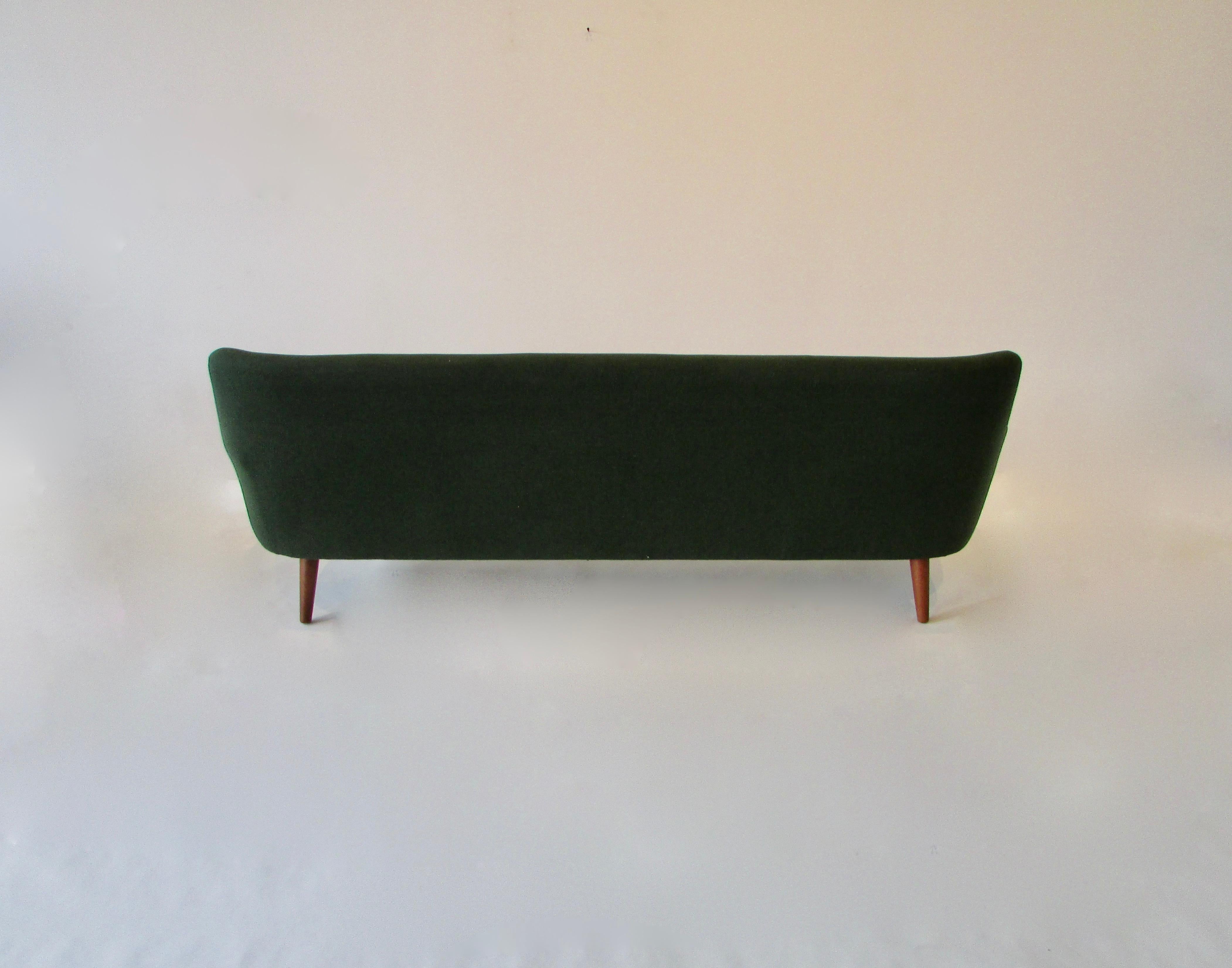 Danish couch with teak trimmed arms on thick teak spindle legs. Much in the style of Hans Wegner. Original green wool fabric is fine but foam has desiccated. Turning to powder. All too often I restore a couch or chairs only to sell and ship to