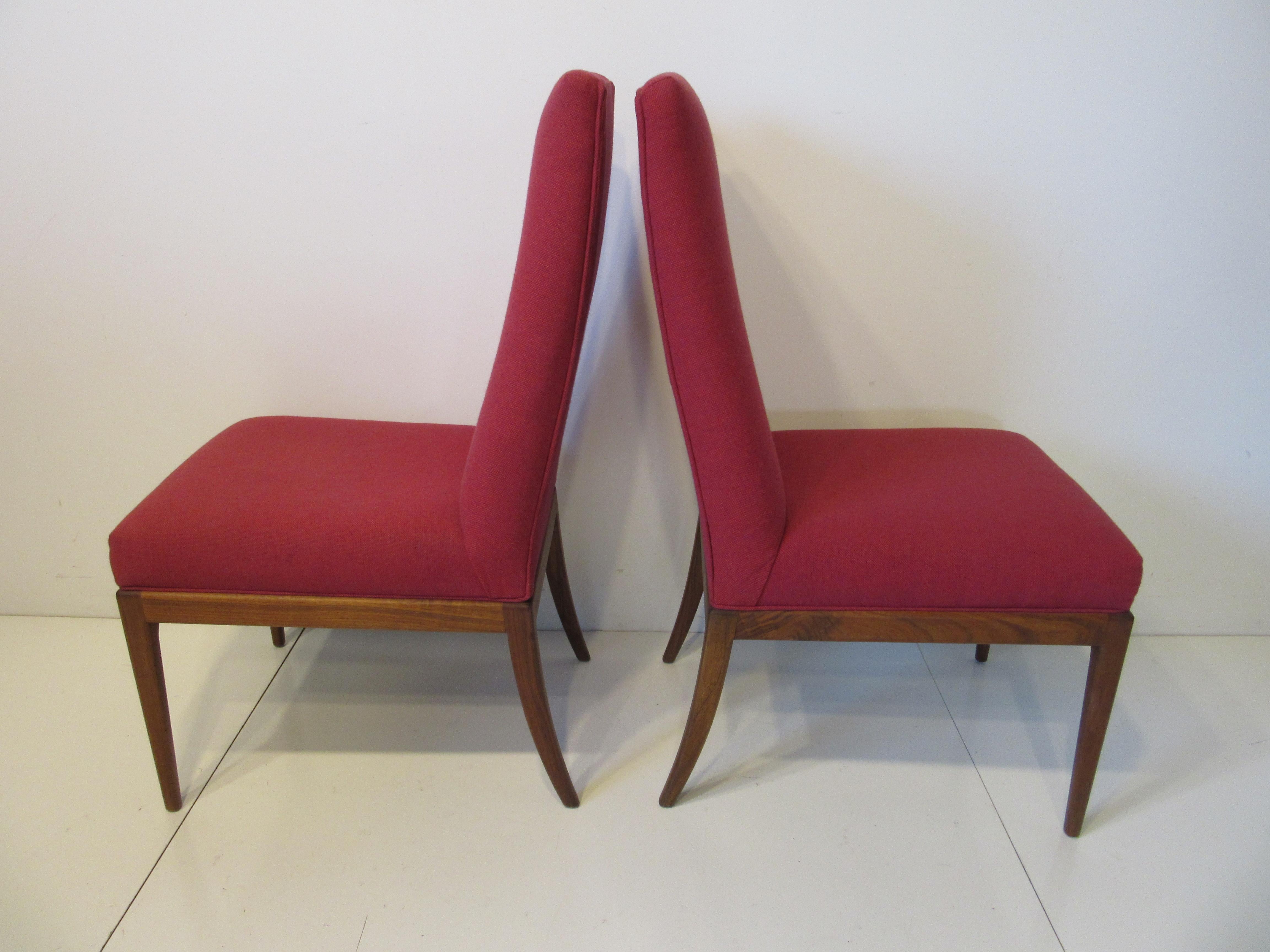 A pair of head dining chairs upholstered in a tightly woven cranberry Danish styled fabric having teak wood frames and saber rear legs. These chairs would work with any modern Danish dining set or could just be used as accent side chairs.