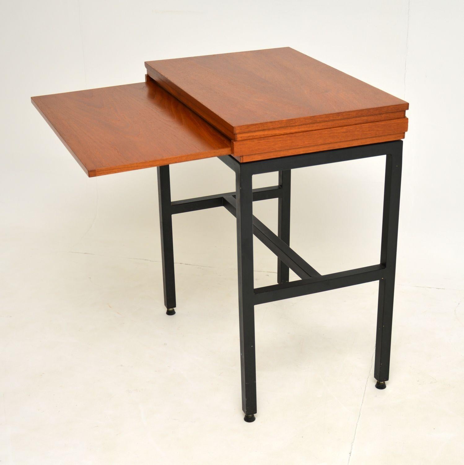 An unusual and stylish side table in teak with an ebonised metal base and pull out writing slide. This was made in England, it dates from the 1960’s.

It is a great size and beautifully finished on all sides, so can be used as a free standing