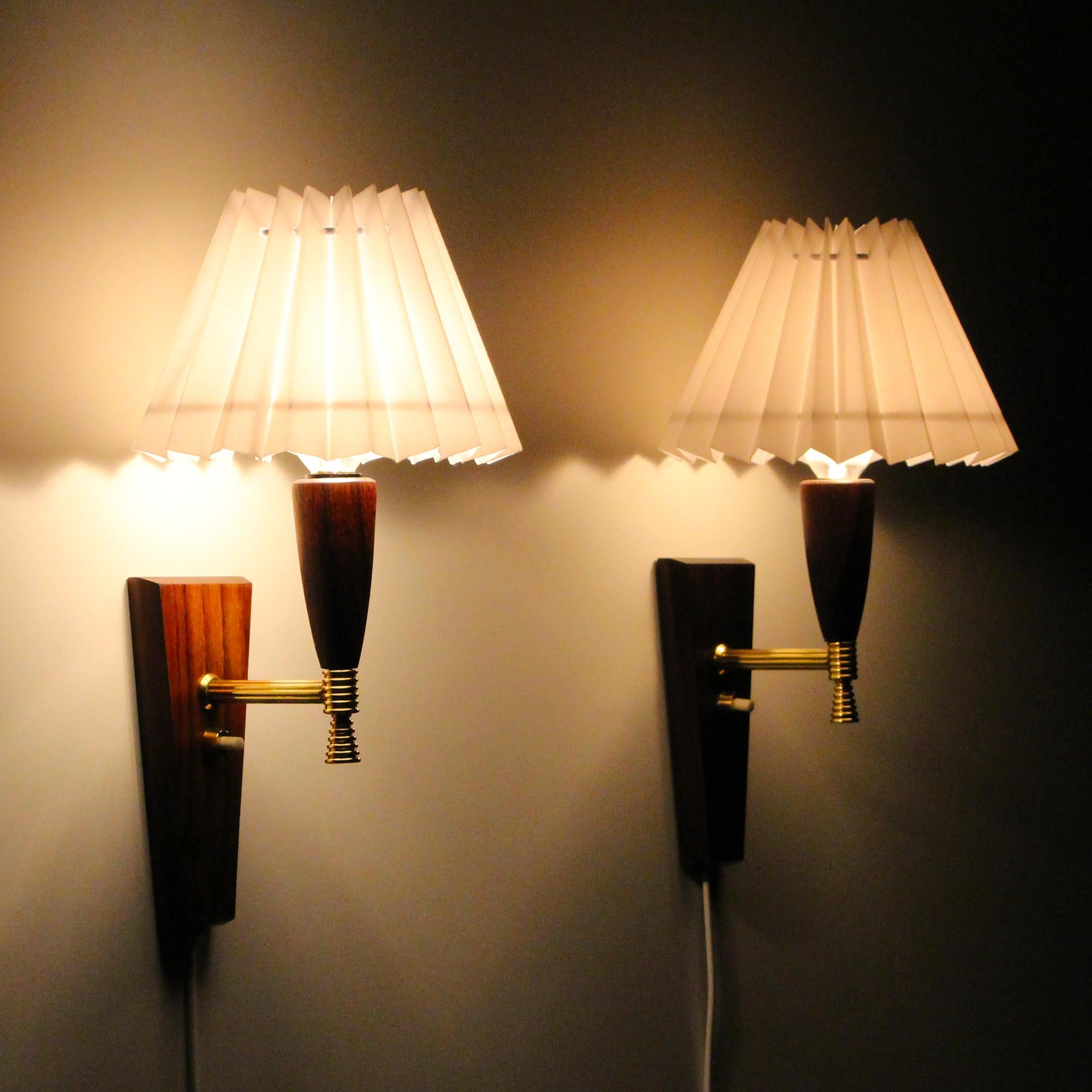 Teak wall lights, pair of 1960s Danish wall lamps with new white pleated shades by Laoni Belysning, in very good vintage condition.

A charming pair of midcentury sconces with trapezoid shaped teak bases, polished brass arms and cone shaped teak