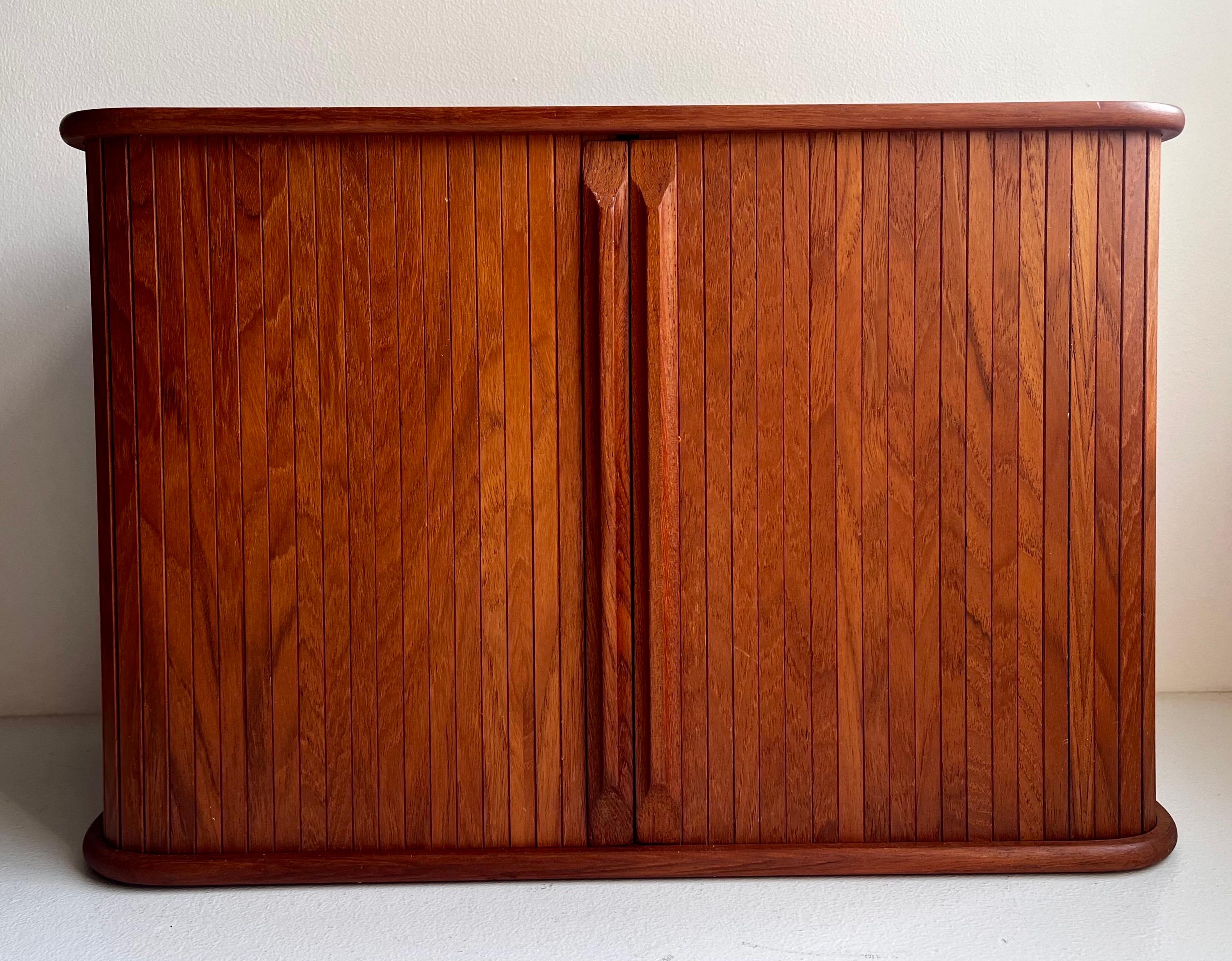 Teak Wall Mounted Storage Cabinet
circa 1970
Manufacturer Stamp on the Back

Unique floating wall mounted storage cabinets.
Easily mounted.
Teak with tambour sliding doors.
Two storage areas on the interior with sliding dividers.
Shelves have