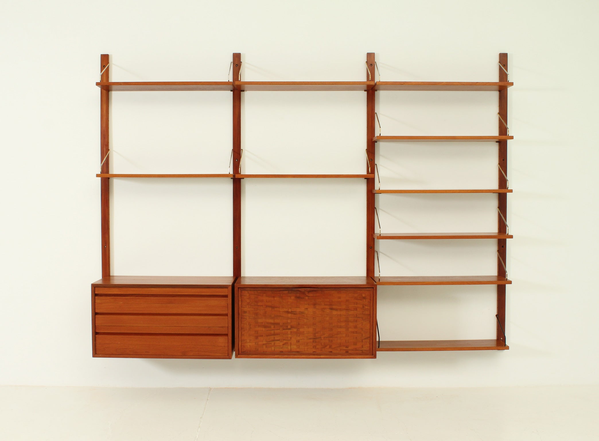 Royal system shelving unit designed in 1948 by Poul Cadovius for Cado, Denmark. Teak wood with brass fittings. One drawer unit with four drawers and one cabinet with folding door with one small drawer inside. Nine shelves 24 x 80 cm. and one shelf