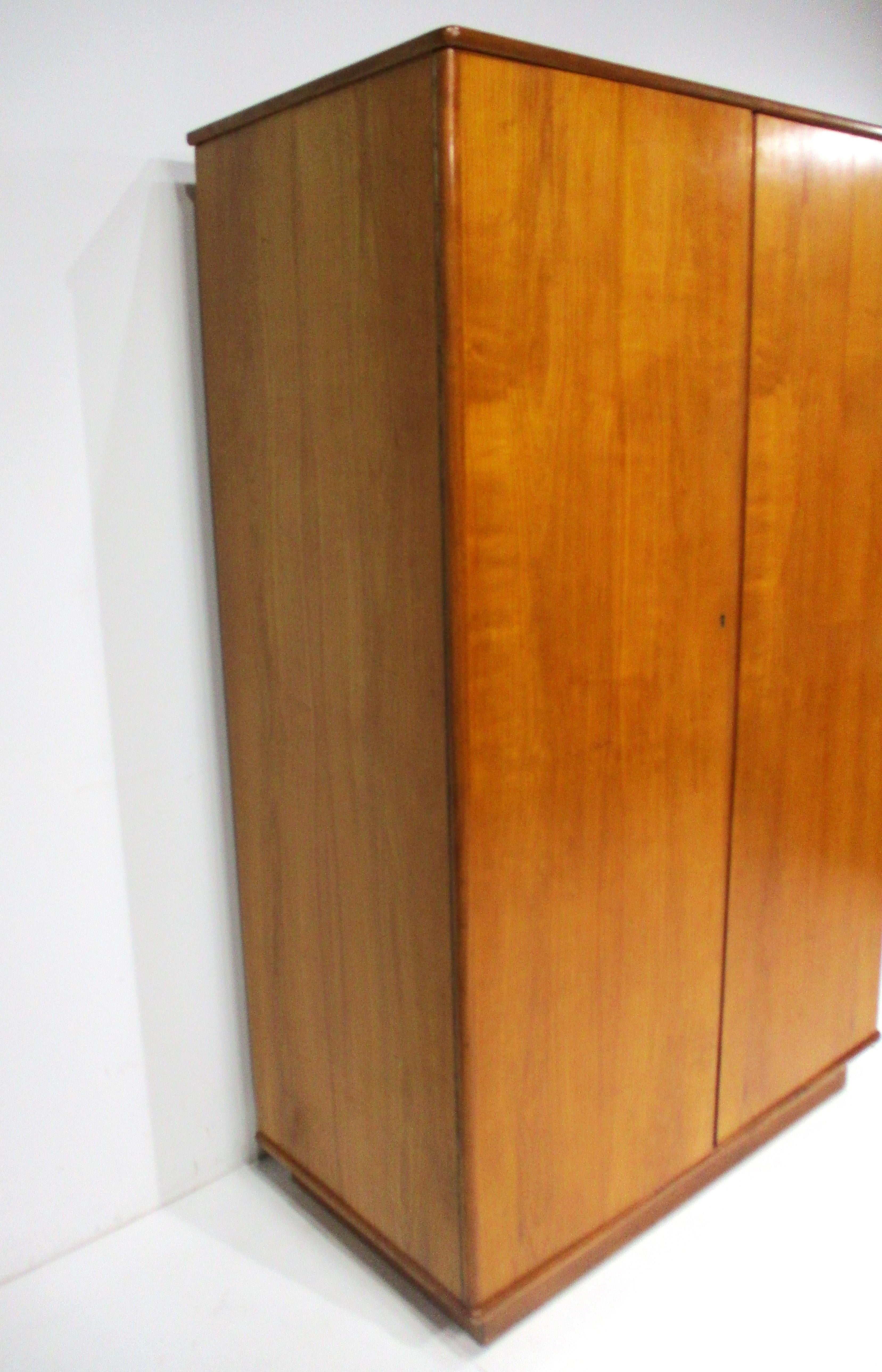 A teak wood double door wardrobe or armoire with brass piano hinges , one large upper shelve with brass hanging rod for hanging clothes and the bottom space for storage . A very functional piece that is great for an area that has limited storage