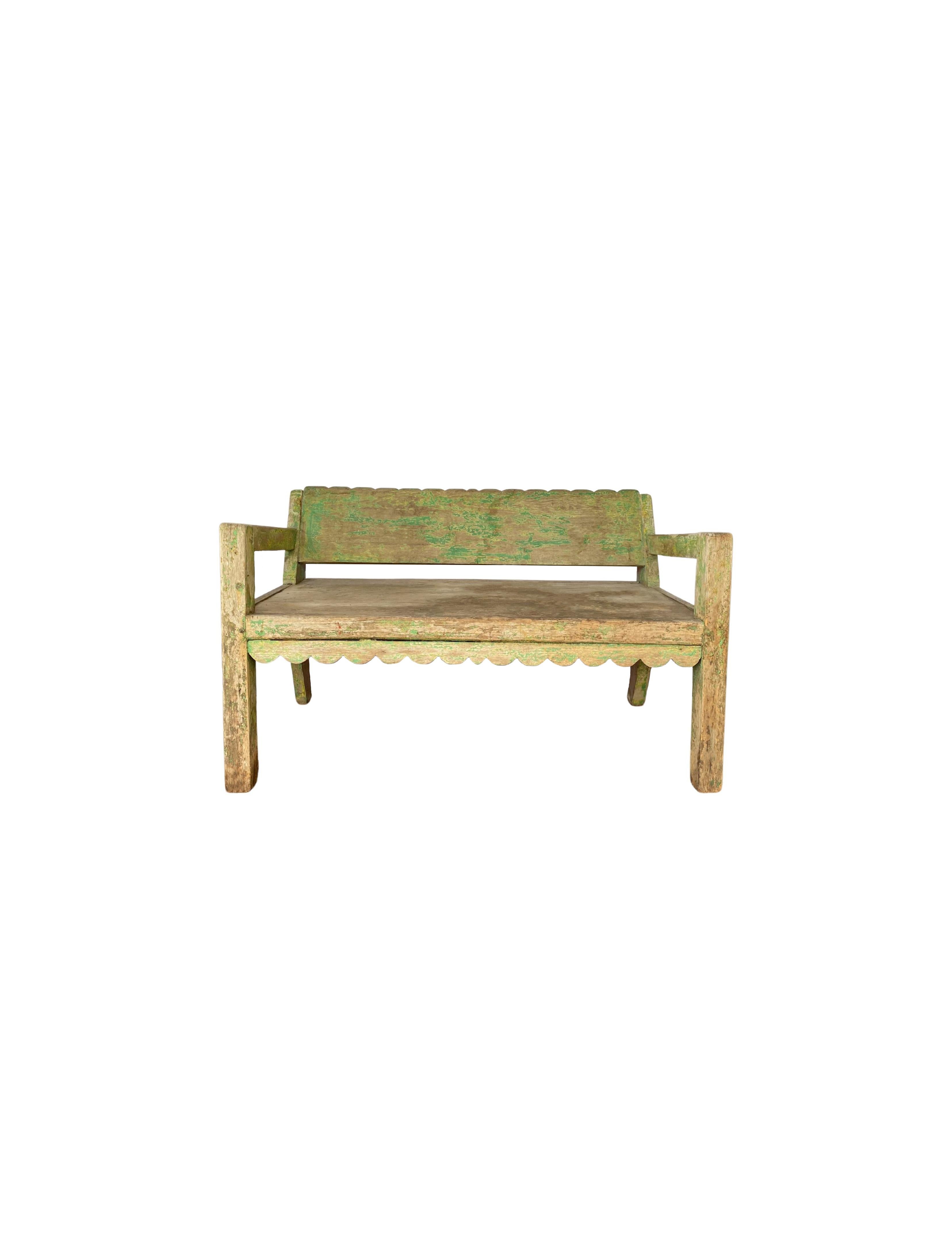 This hand-crafted teak wood low bench originates from the Island of Madura, off the coast of Northeastern Java. It features subtle carved detailing on the backrest as well as a wonderful green polychrome. The fading of the polychrome and age-related