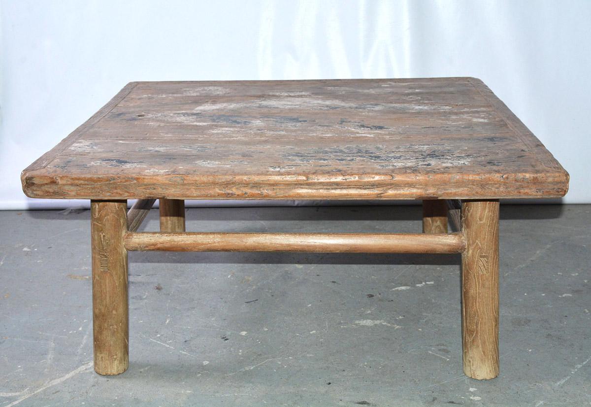 The rustic almost square country style Asian teak wood coffee table has rounded legs and stretchers with solid pegged construction. The plank top is secured by breadboard ends. The rusticity of the table lends itself to informal living indoors or on