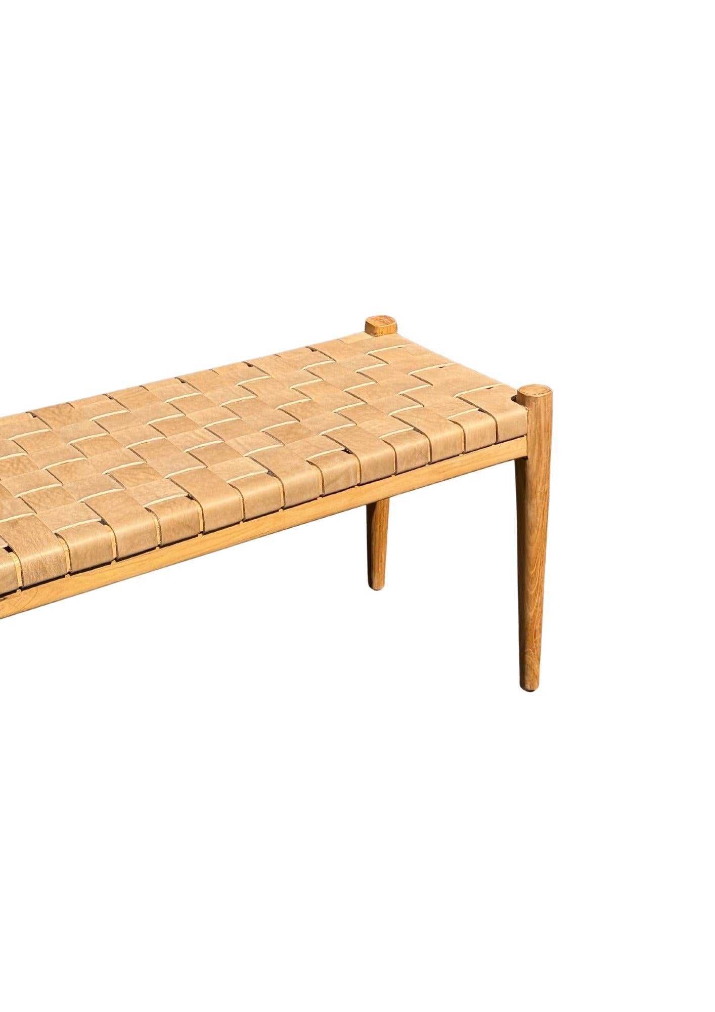 Banc artisanal avec cadre en teck et sangle en cuir tressé. Ces bancs sont fabriqués par des artisans locaux qui utilisent une technique d'assemblage du bois sans utiliser de clous. Ils présentent une texture boisée subtile et sont robustes.