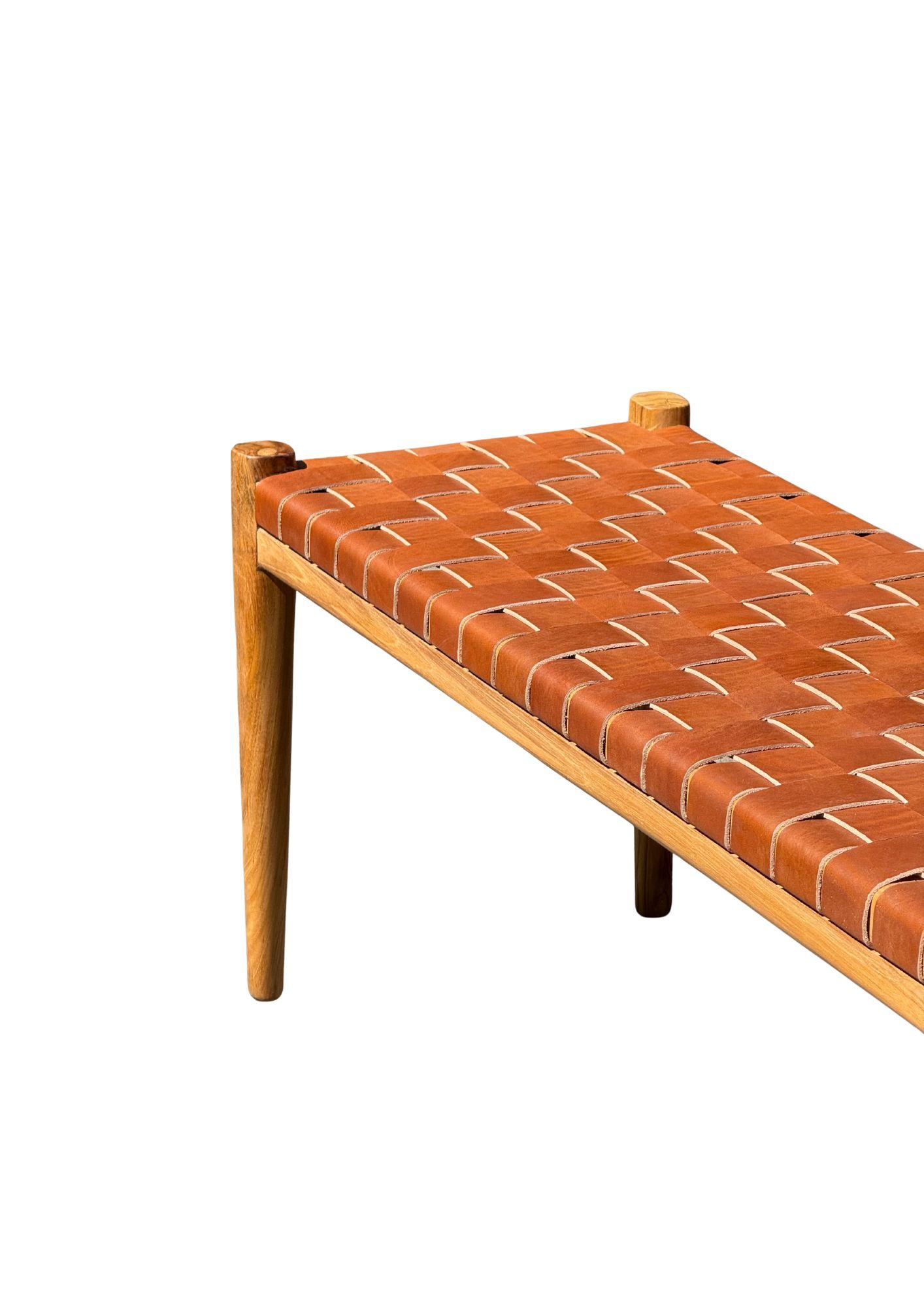 Banc artisanal avec cadre en teck et sangle en cuir tressé. Ces bancs sont fabriqués par des artisans locaux qui utilisent une technique d'assemblage du bois sans utiliser de clous. Ils présentent une texture boisée subtile et sont robustes.